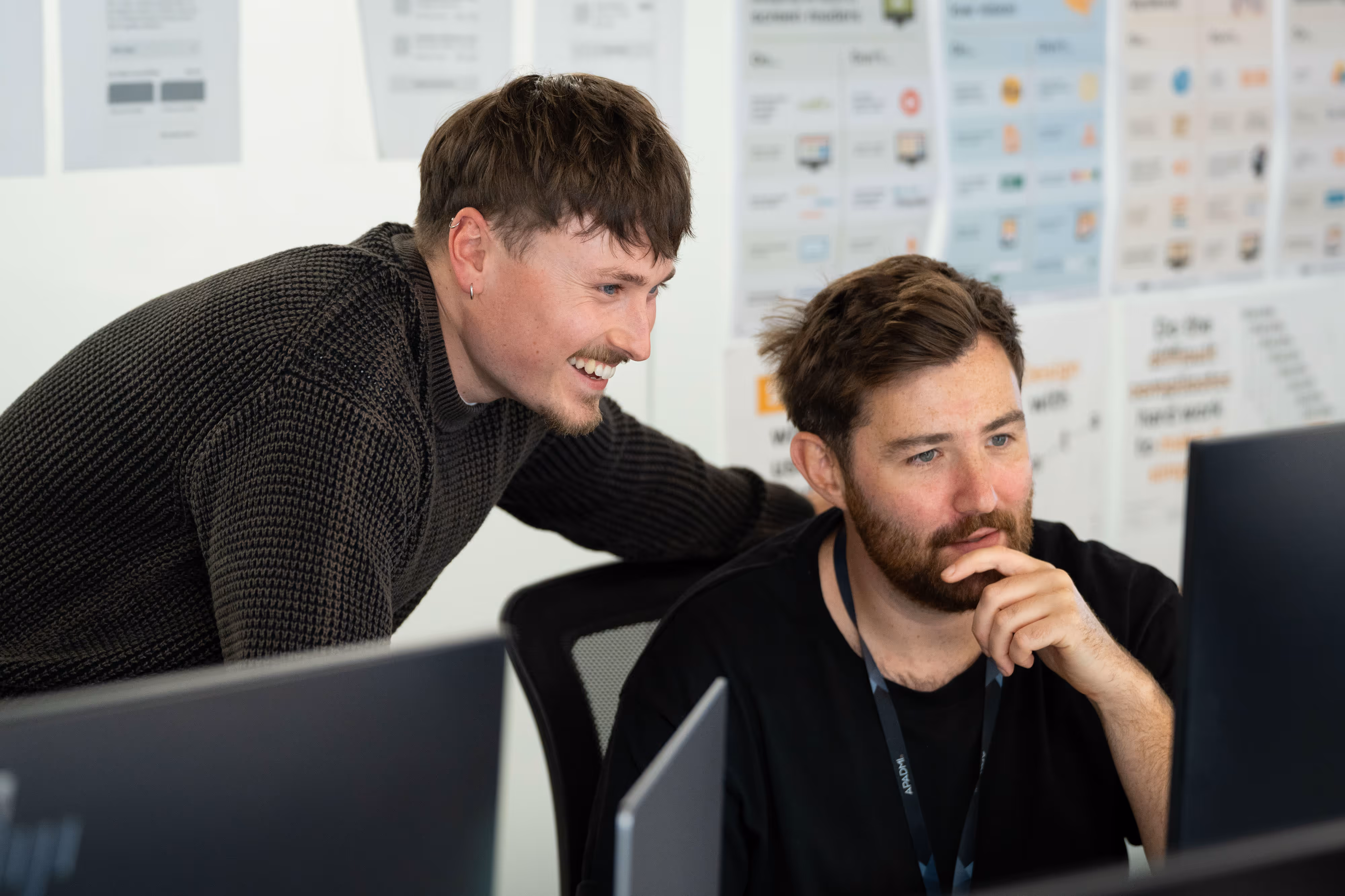 Two developers chatting whilst looking at a computer screen in a bright Media City office.