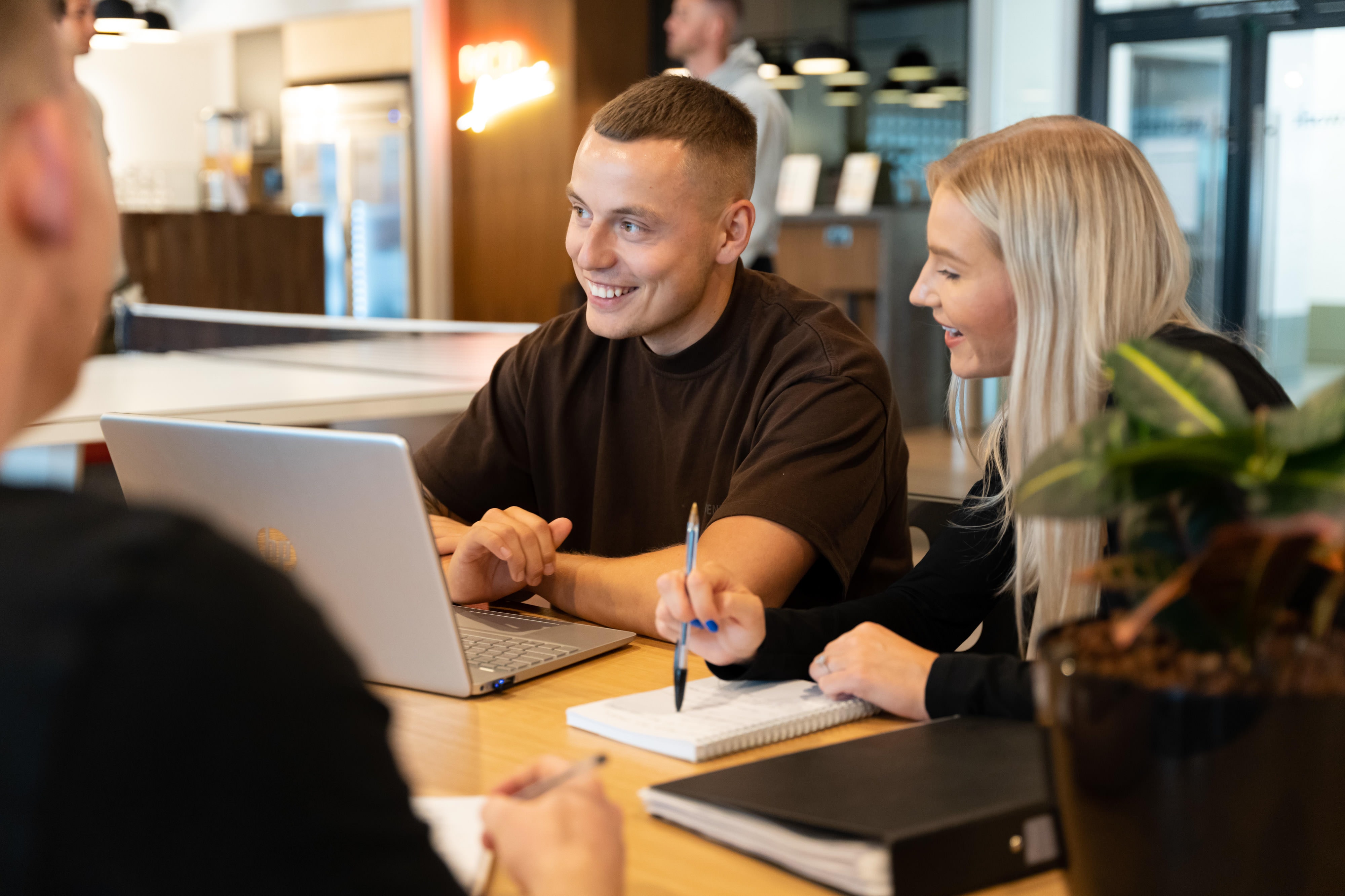 Two people smiling whilst working together at a table with a laptop and notebooks in a WeWork office in Spinningfields.