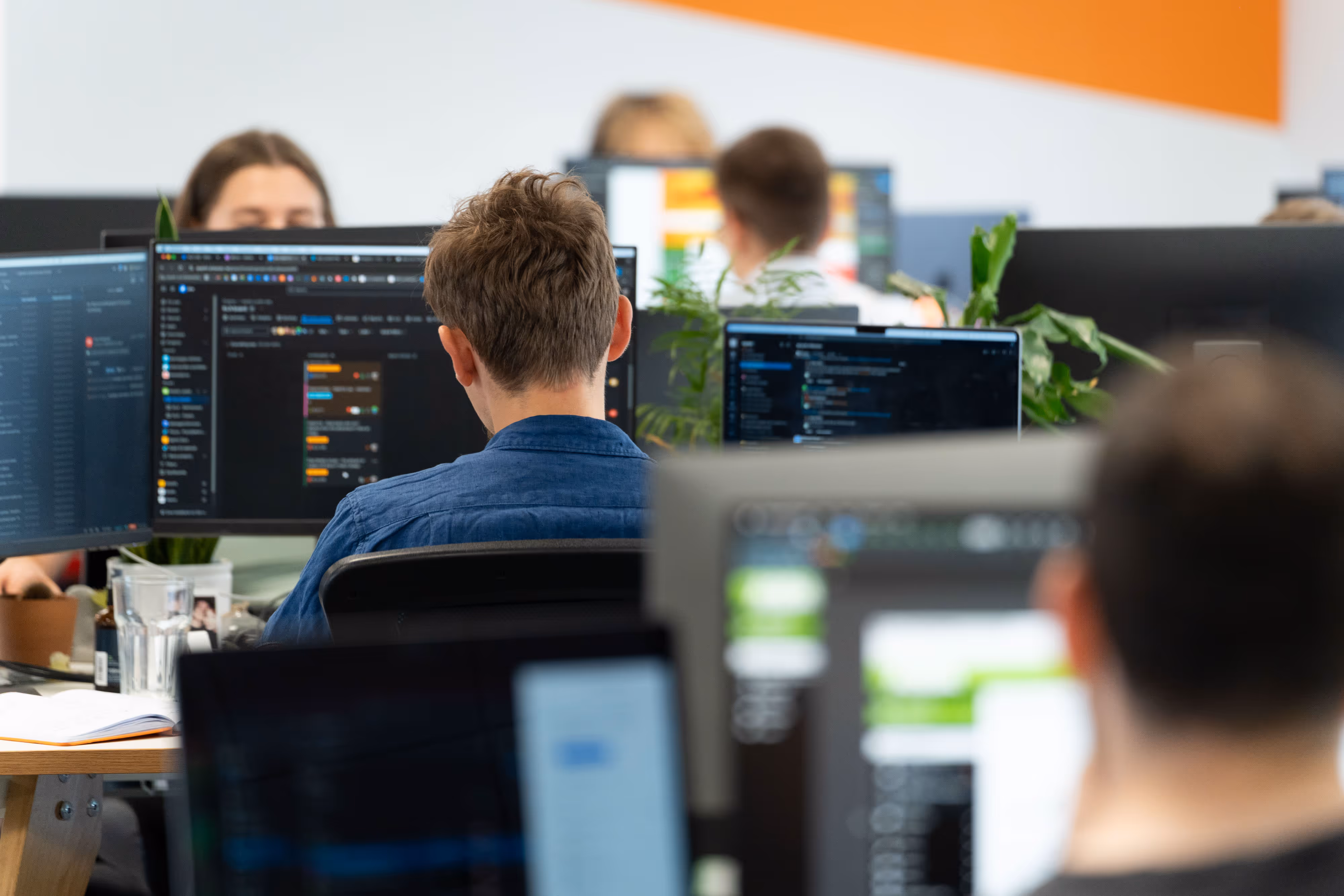 People working at computer desks in an open-plan office of an app agency, with code visible on several computer monitors.