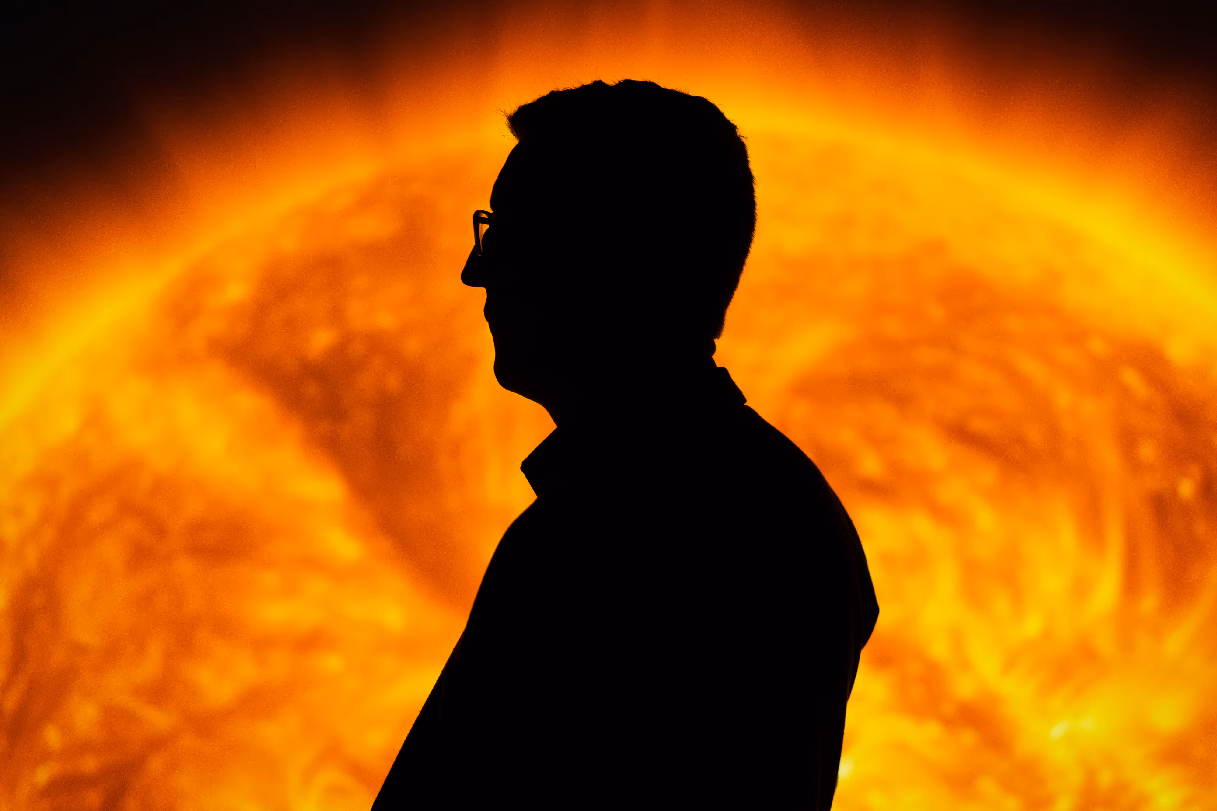 Silhouette of a person in glasses in front of a vivid, fiery sun backdrop at a museum exhibit in Bradford.