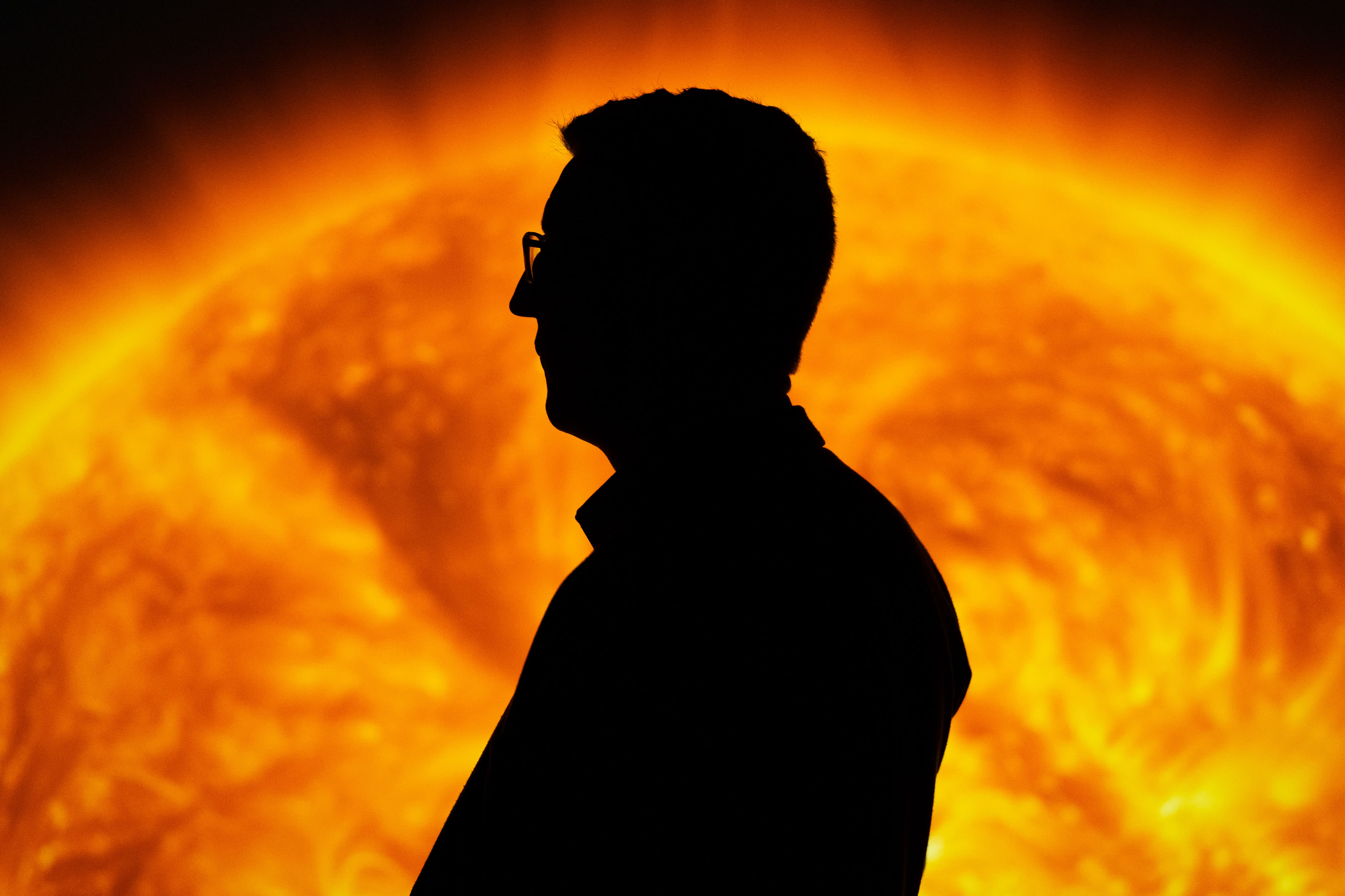 Silhouette of a person in glasses in front of a vivid, fiery sun backdrop at a museum exhibit in Bradford.