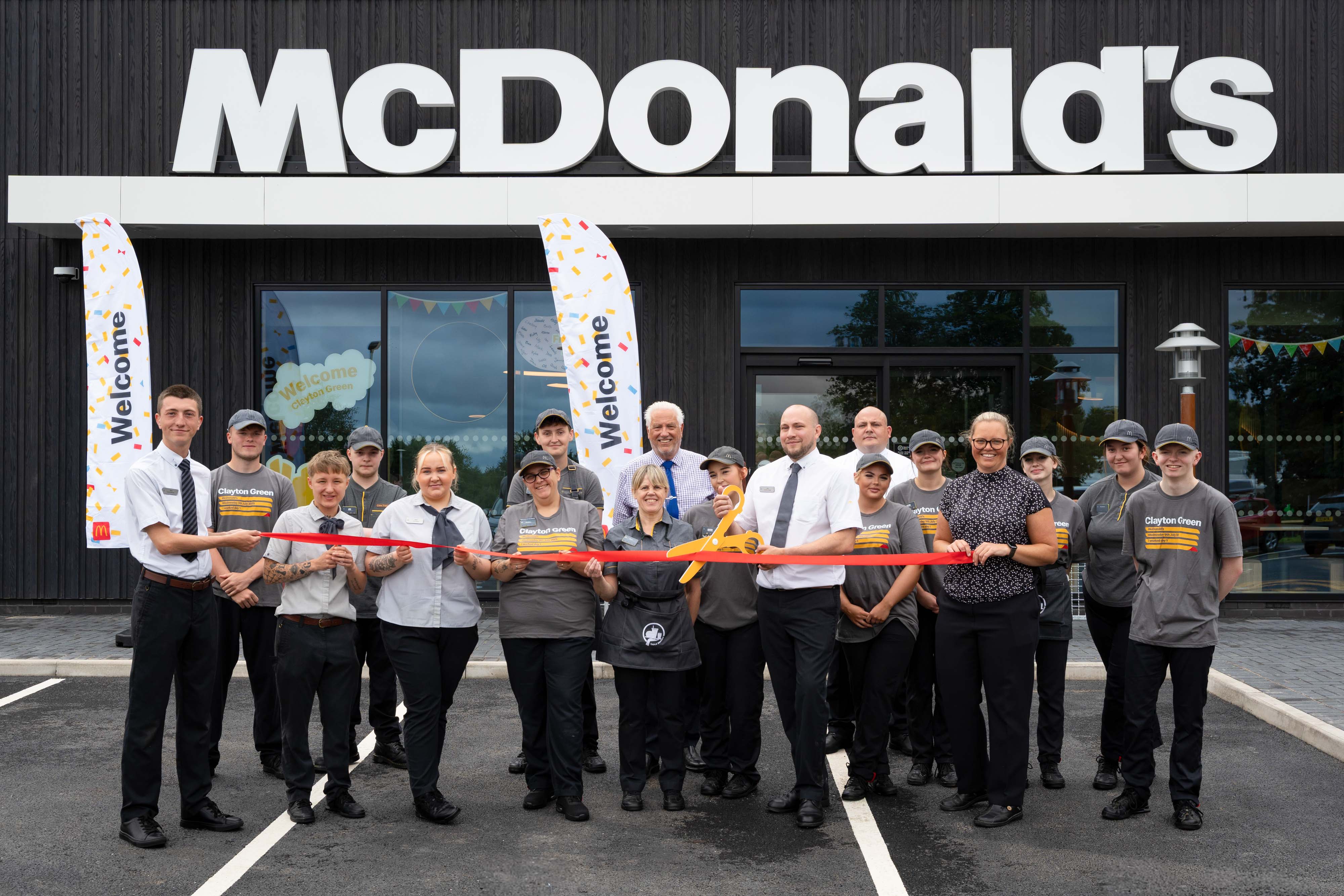 A group of McDonald's employees and managers cutting a red ribbon outside a McDonald's restaurant.