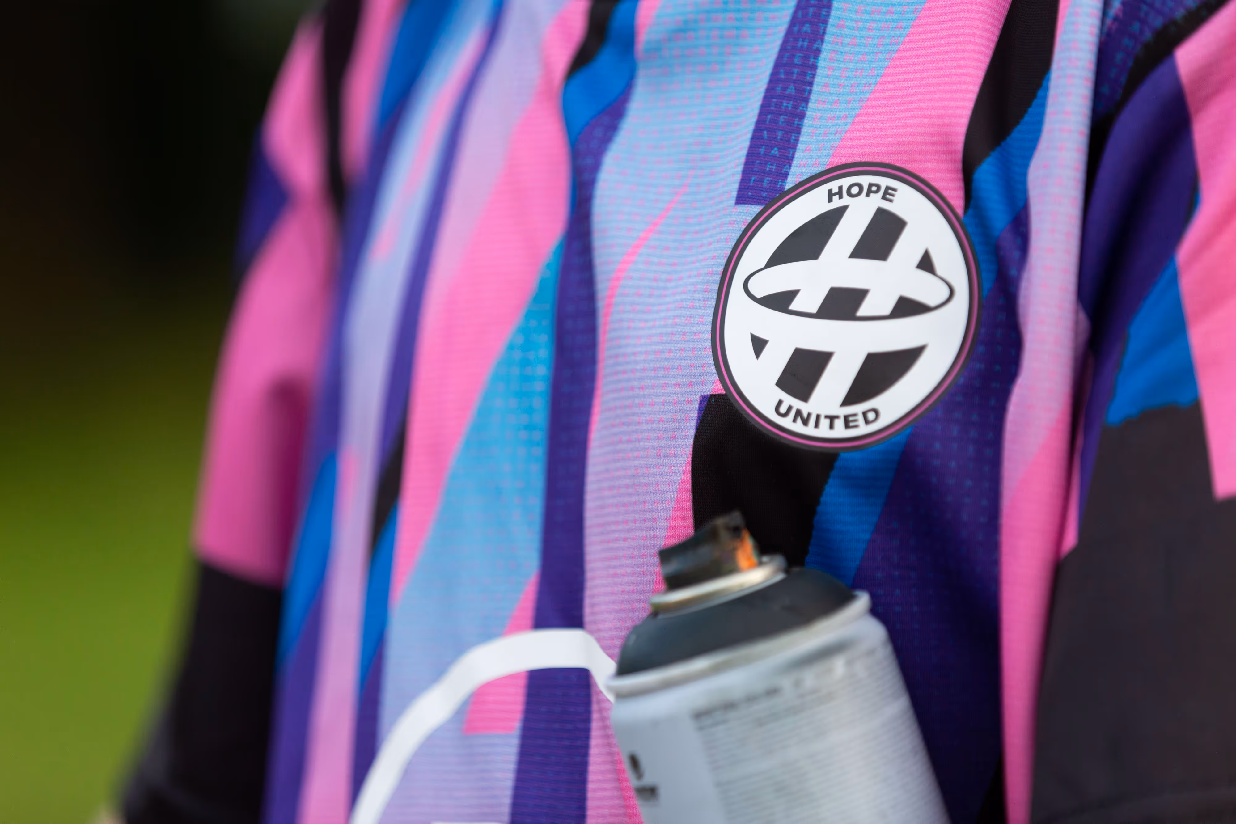 A person in a colourful jersey with a "Hope United" badge holds a spray paint can.