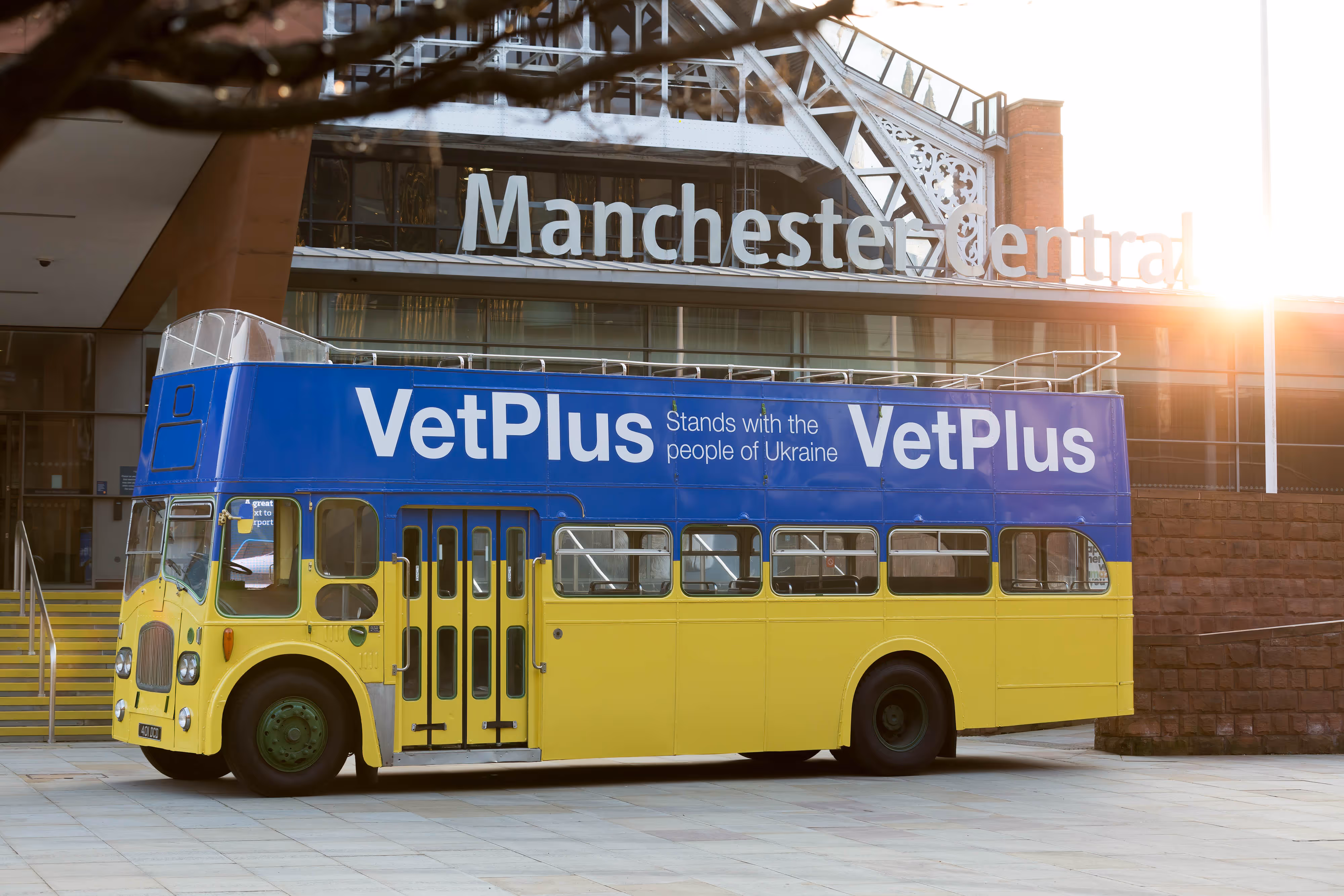 A blue and yellow double-decker bus with "VetPlus" parked as a PR stunt outside Manchester Central.