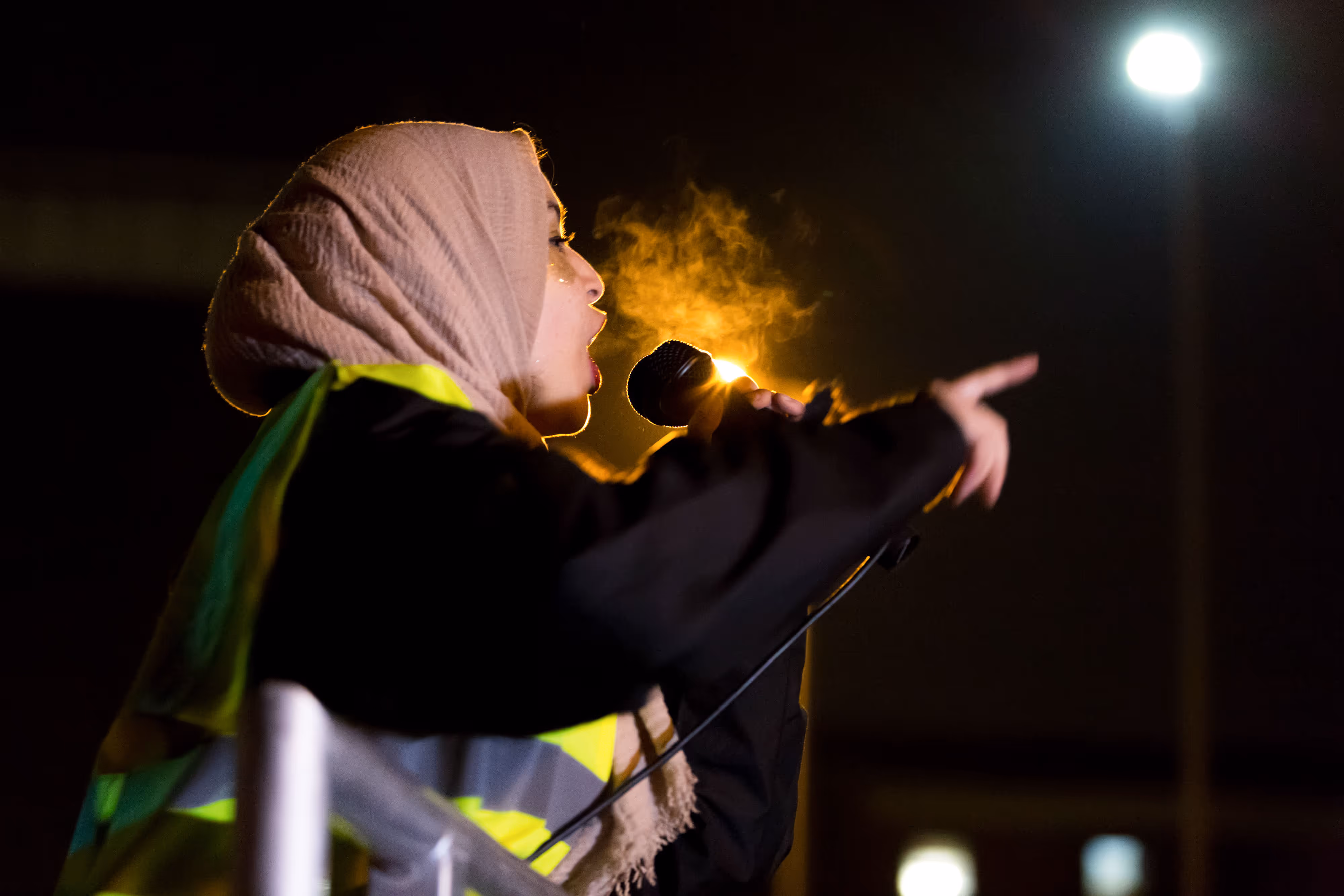 A woman speaking into a microphone at a public protest on Oxford Road in Manchester.