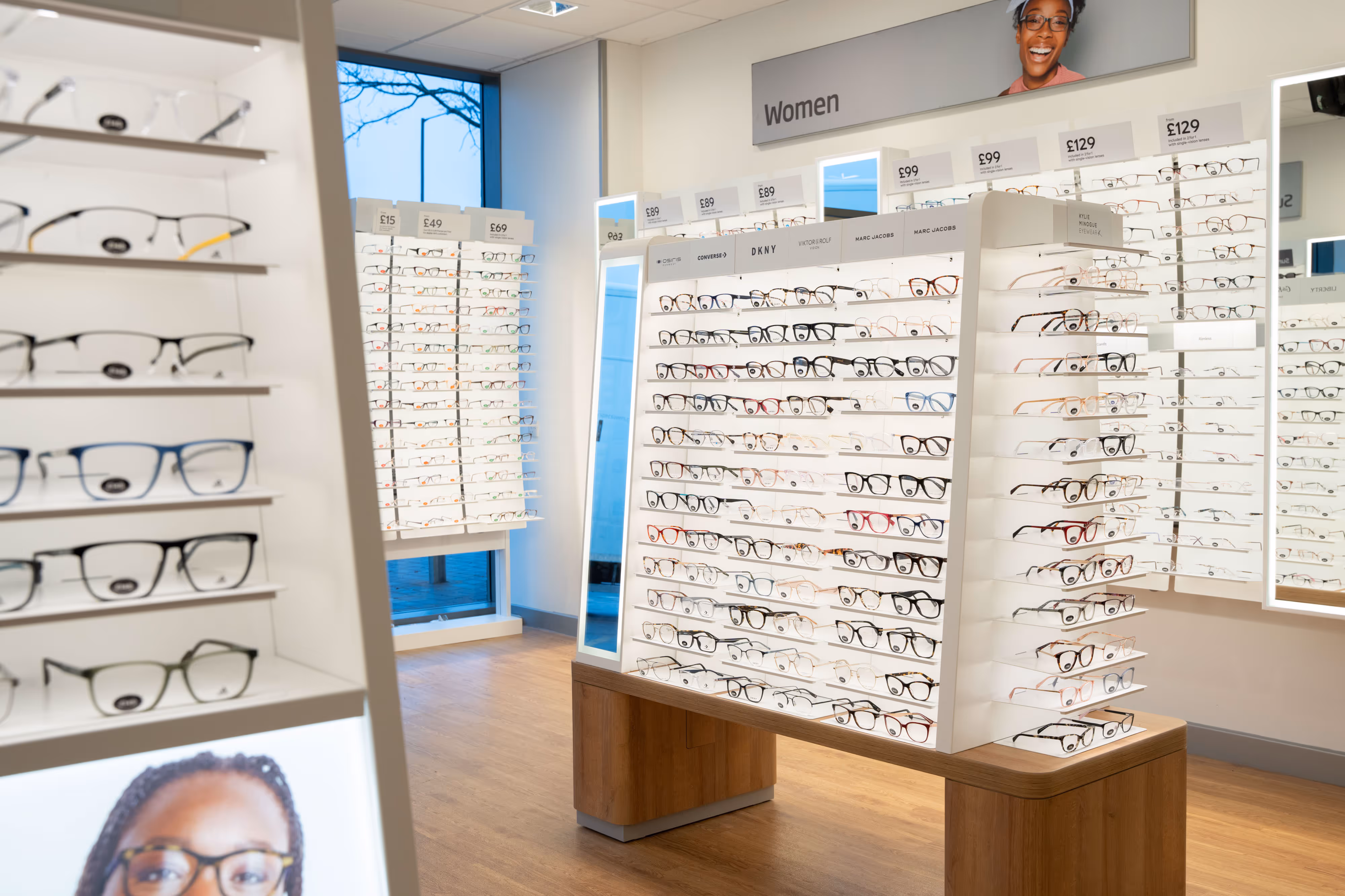 Display area in an optician's shop with rows of women's spectacle frames on white shelves.