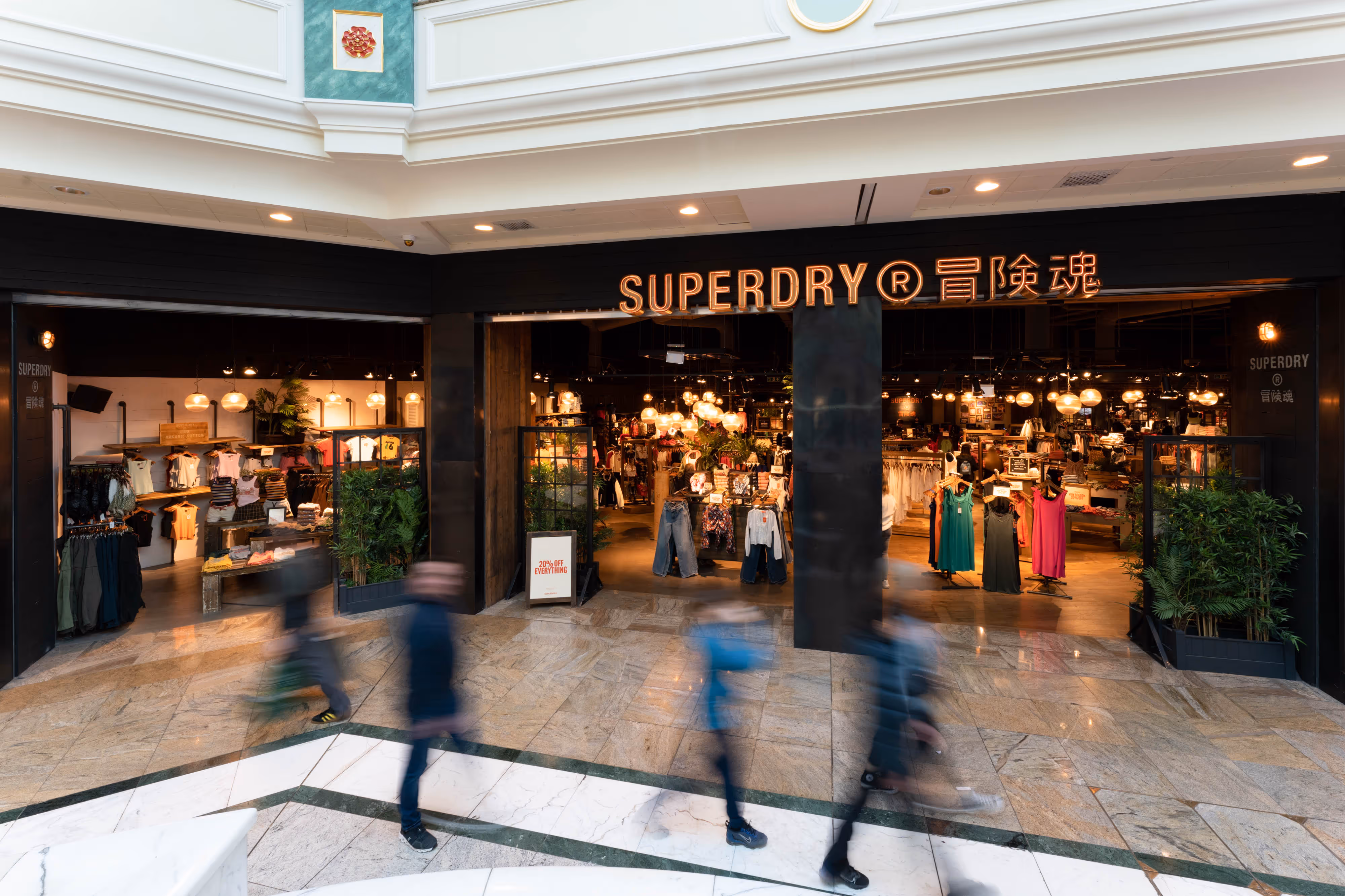 Exterior shot of a Superdry shop in a shopping centre, with blurred people walking past the entrance.