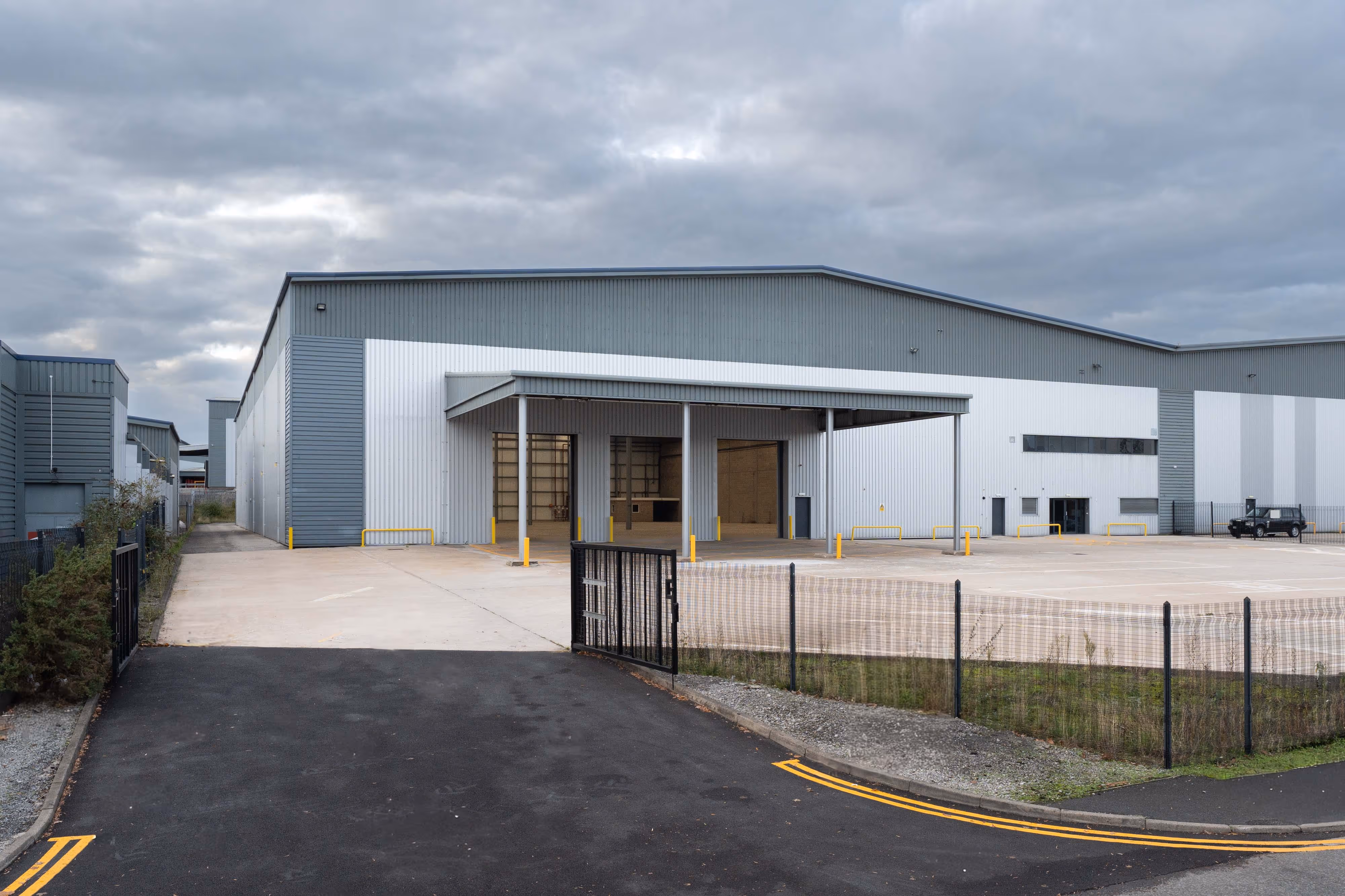 Large, modern warehouse with loading bays, fenced entrance, and cloudy sky overhead.