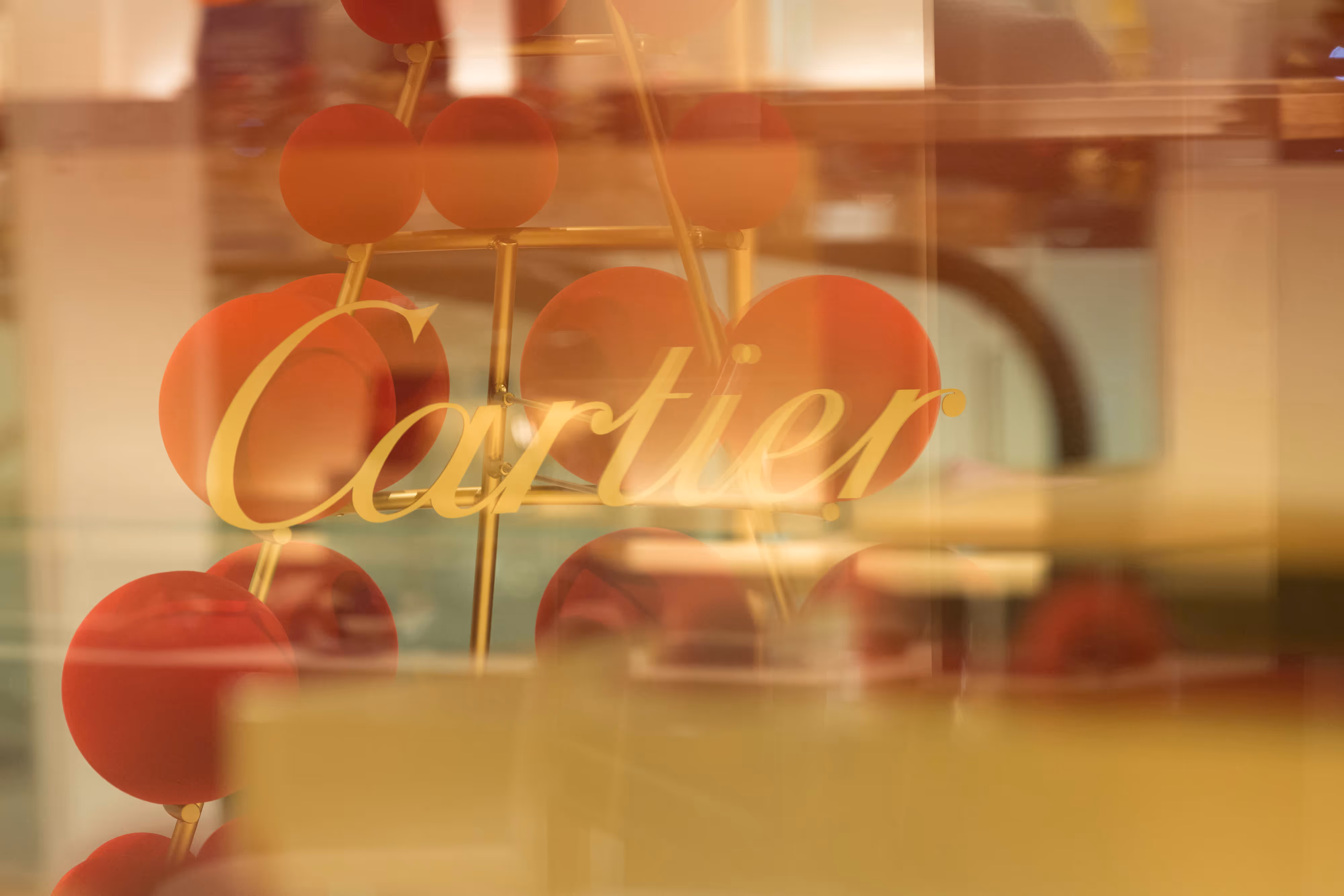 Photographed Cartier signage in refined gold lettering, set against a backdrop of red circular accents in the shop.