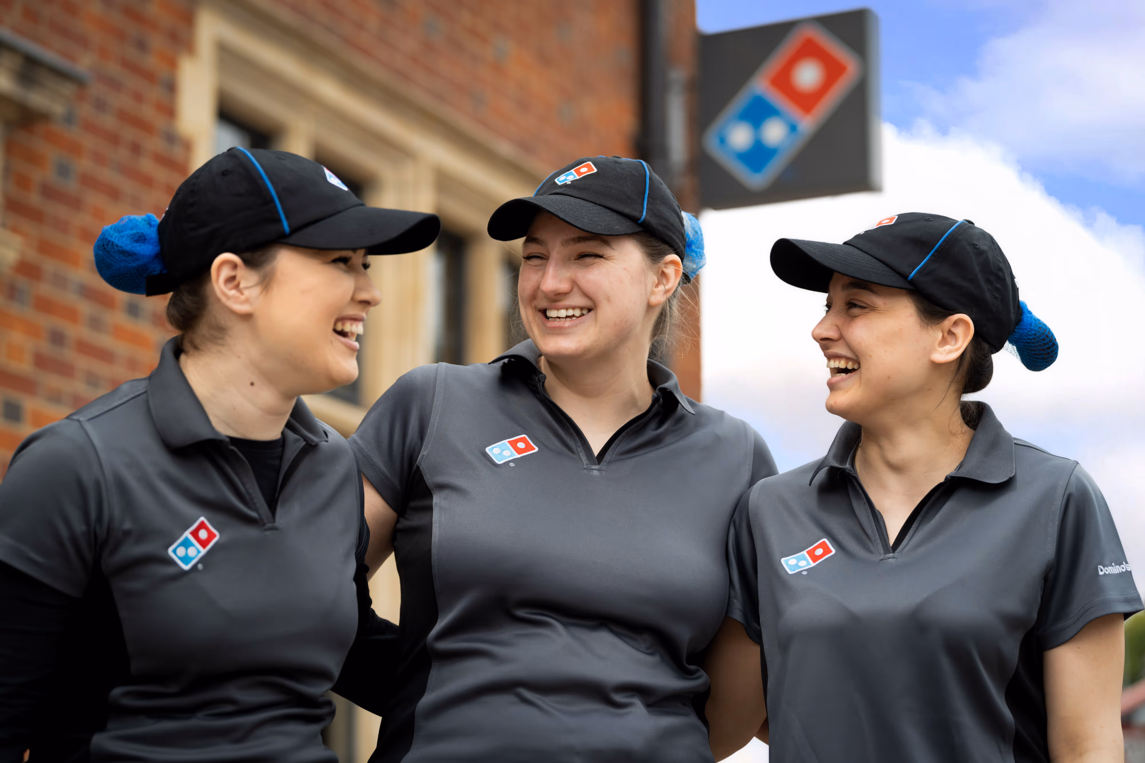 Candid moment of three Domino’s team members in uniform sharing a laugh outside the shopfront, capturing genuine camaraderie.