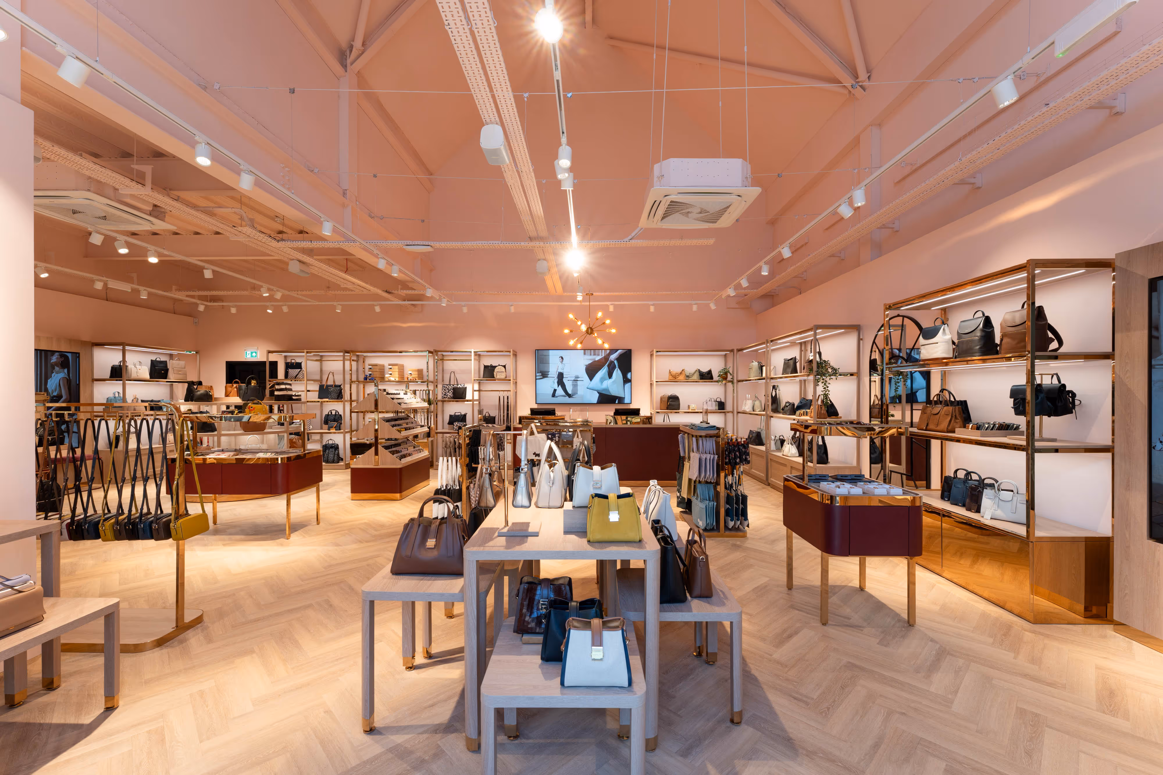 Vibrant boutique interior with pink walls, stylish wooden tables, and neatly arranged shelves of handbags and accessories.
