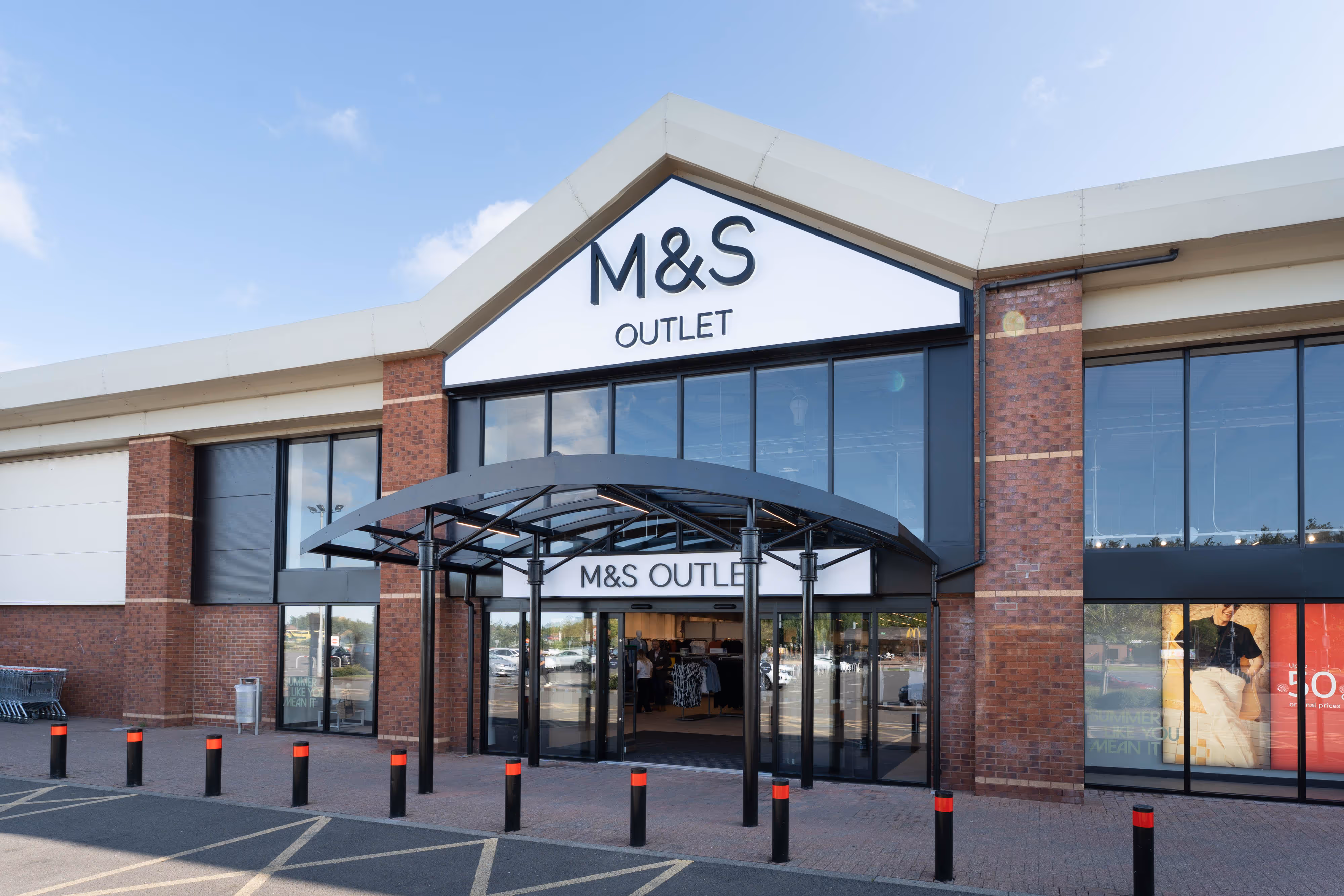 Front view of M&amp;S Outlet shop, capturing glass entrance doors, brick facade, and prominent branded sign for retail portfolio use.