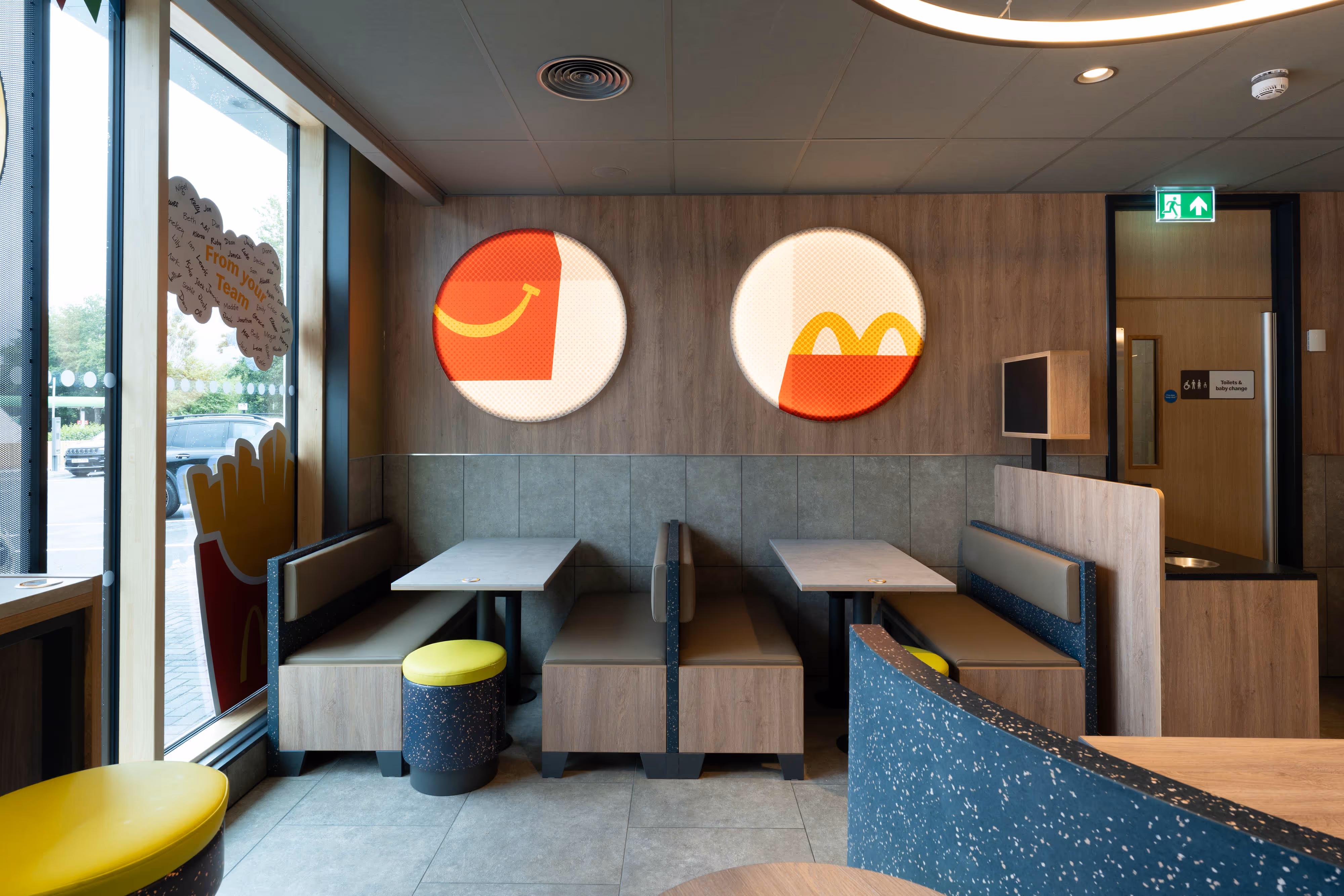 Photograph of a fast food restaurant's seating area, highlighting wooden tables, stools, and vibrant graphic wall art.
