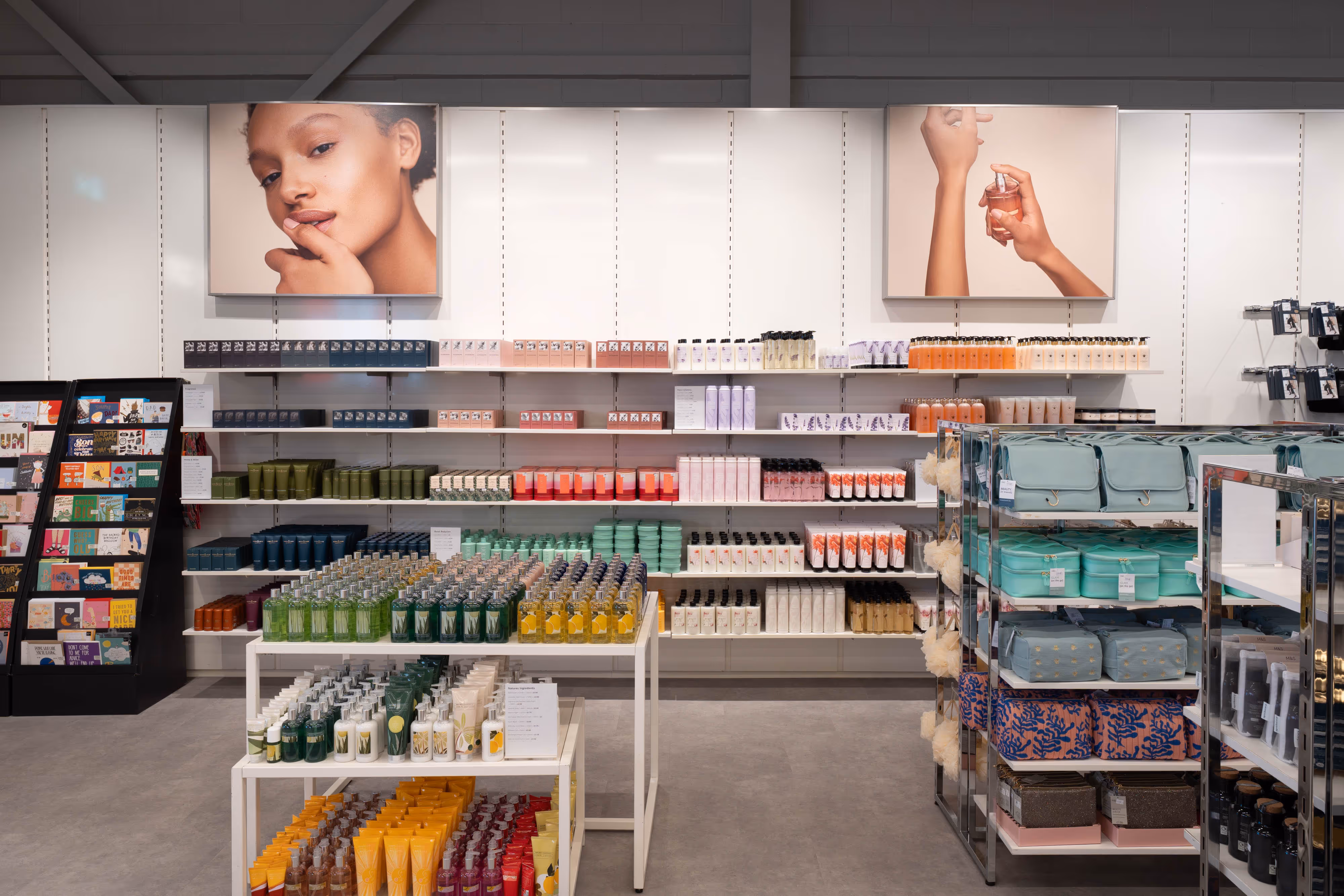 Photographed: shelves neatly arranged with skincare, beauty items, bags, and greeting cards beneath bright product advert posters.