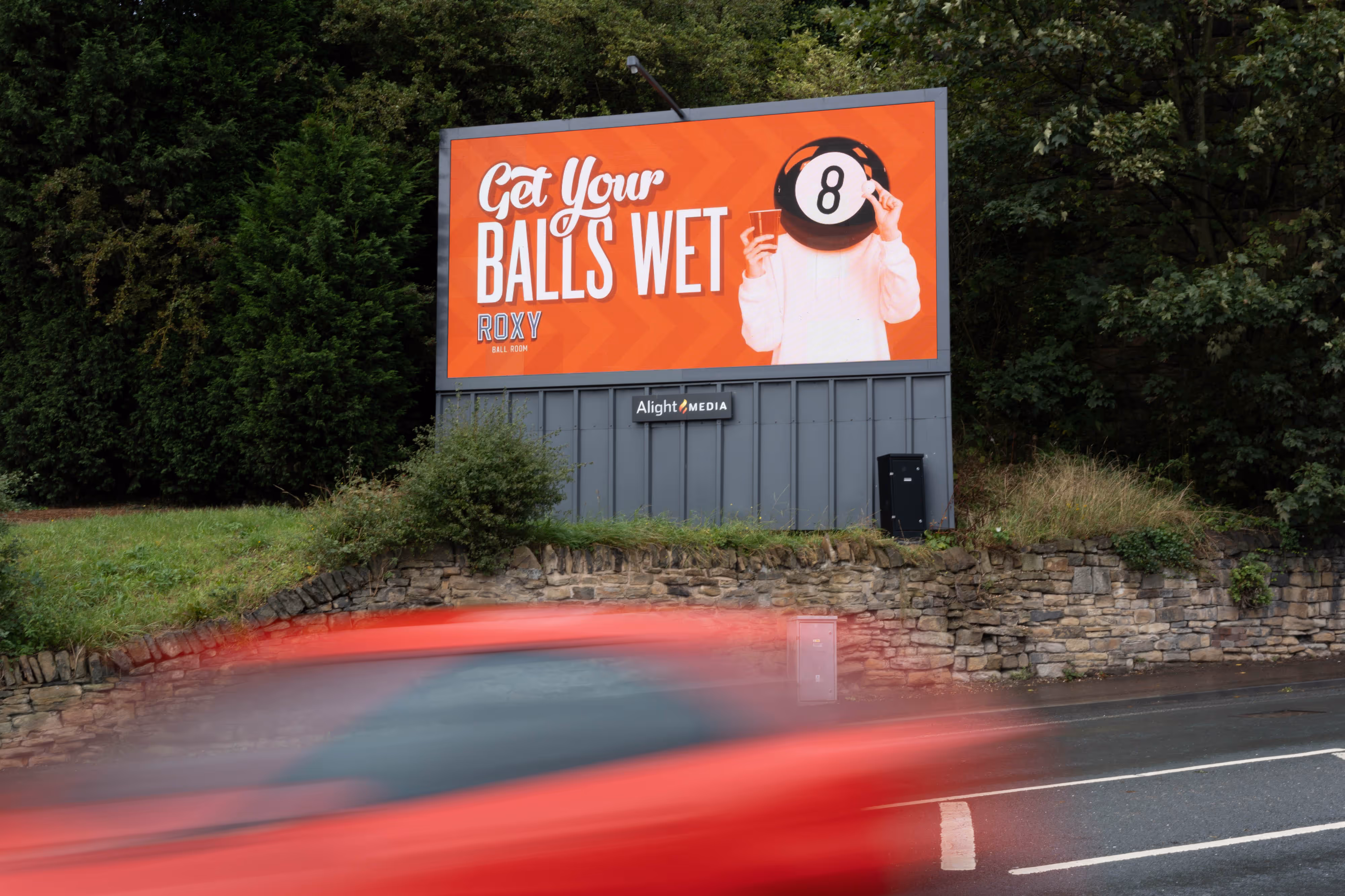 Framed a shot of a red car driving past a striking billboard: “Get Your Balls Wet” beside a person holding a snooker ball to their face.