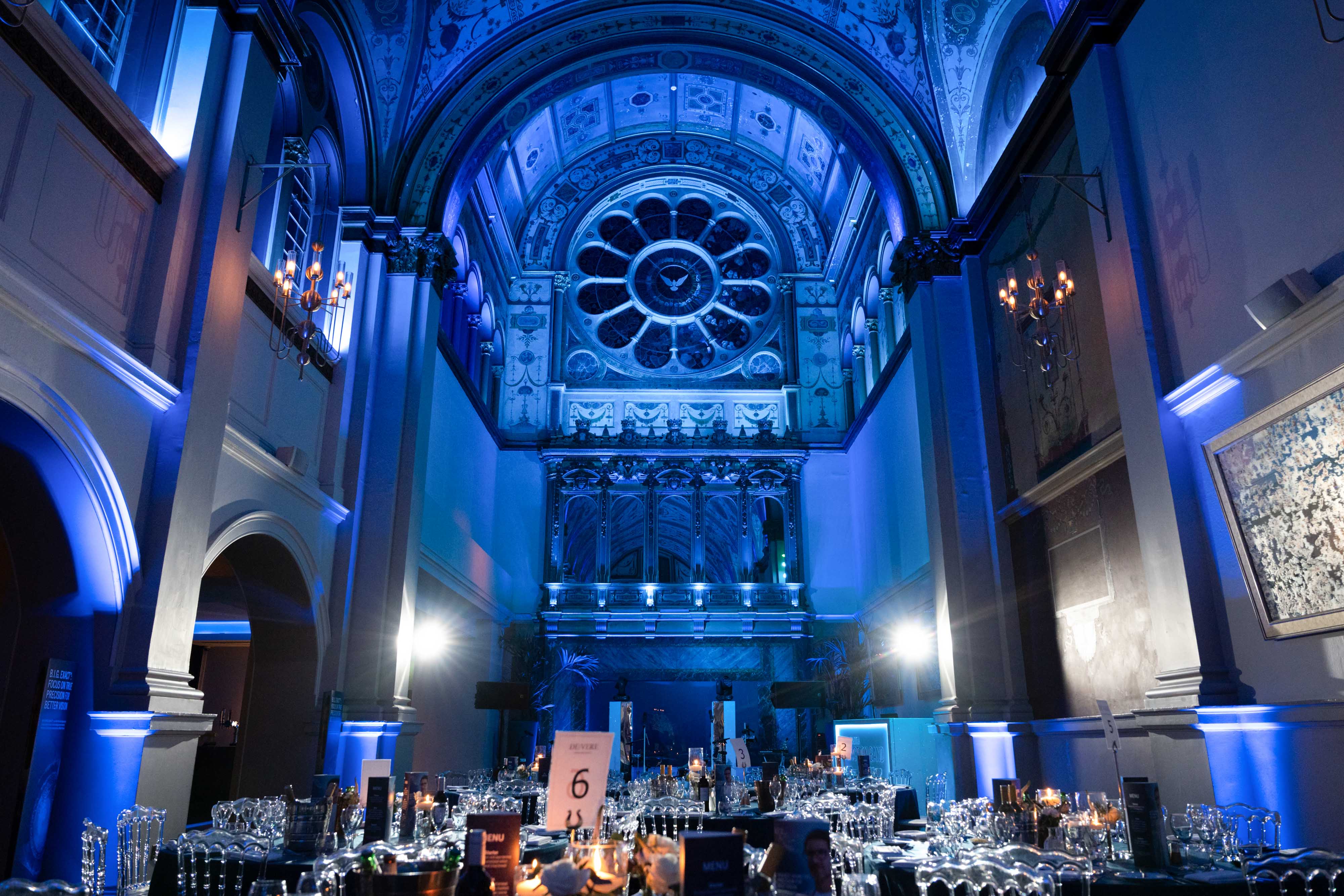 Captured at a corporate Christmas party: a grand hall with arched ceilings, blue lighting, and elegant dining tables.