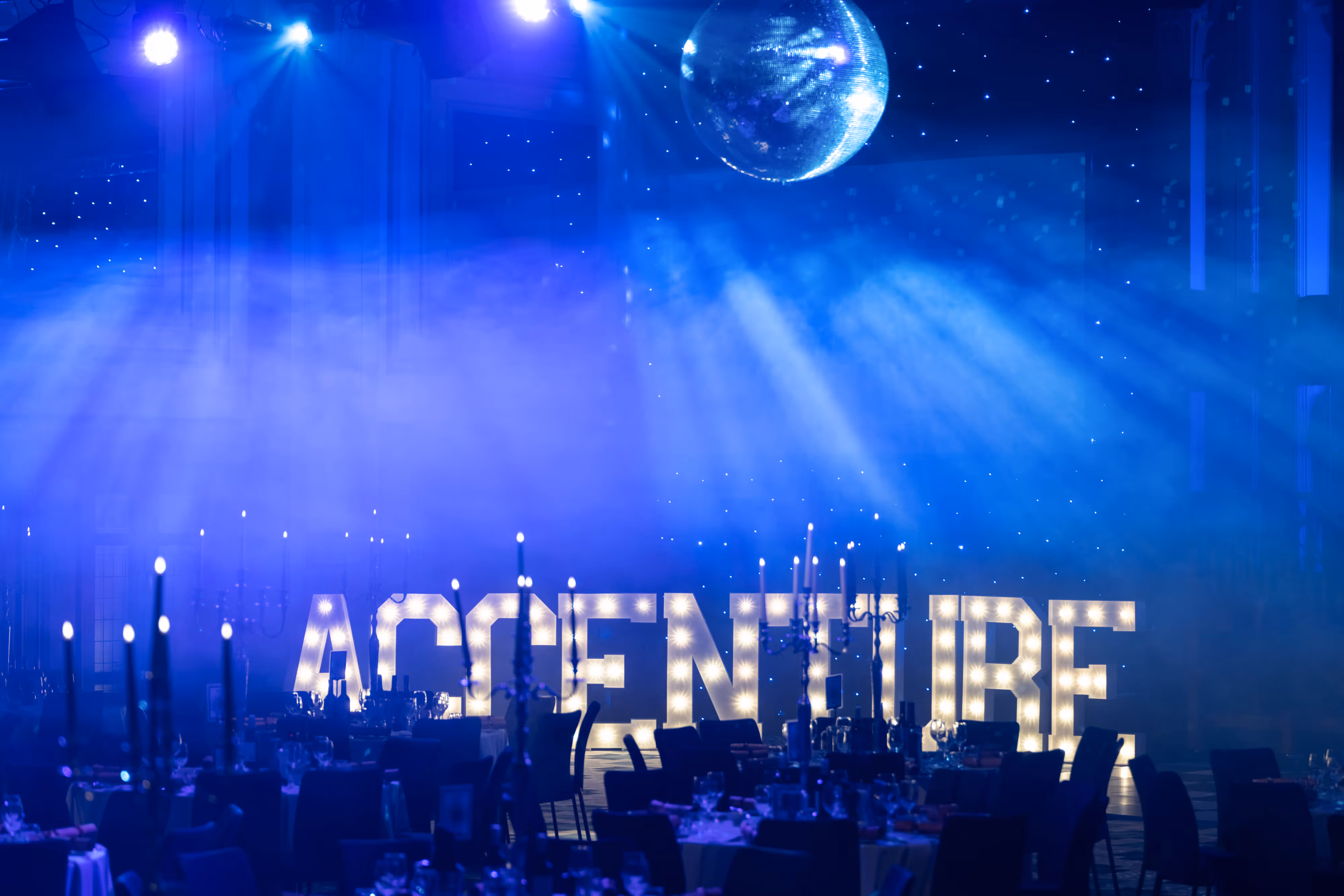 Illuminated "ACCENTURE" letters light up our Manchester event hall, glitter ball shining over festive Christmas party dinner tables.