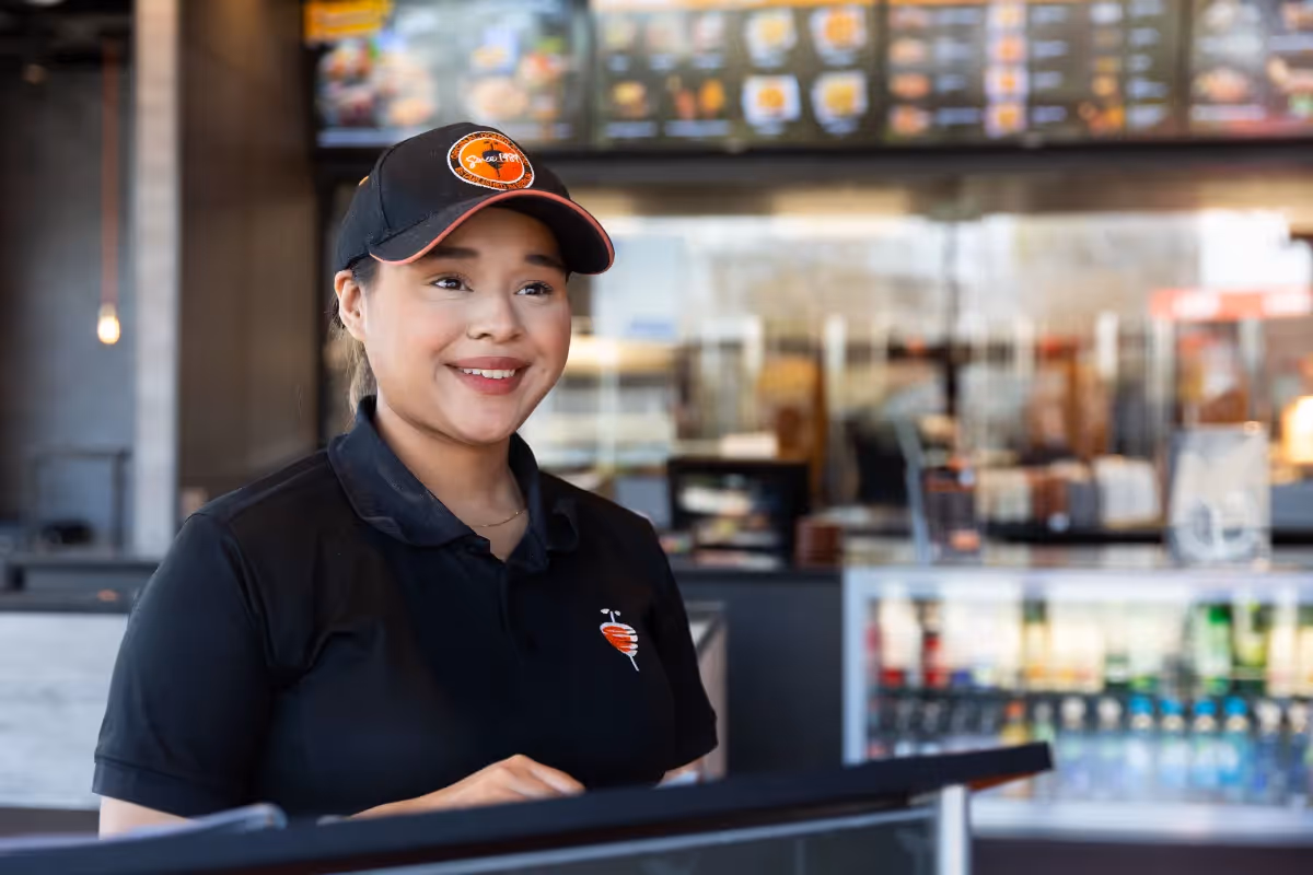 Portrait of a smiling fast food worker in uniform at the counter, poised to assist customers in a brightly lit restaurant.