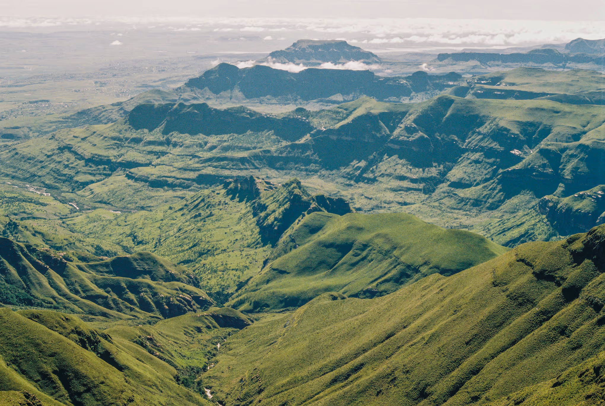 Wide aerial view of lush green rolling mountains under a partly cloudy sky.