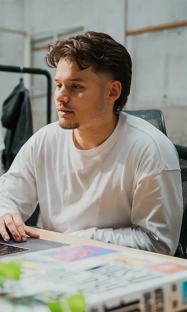 Victor van East Creatives aan het werk achter zijn bureau in een creatieve studio, gekleed in een witte trui.