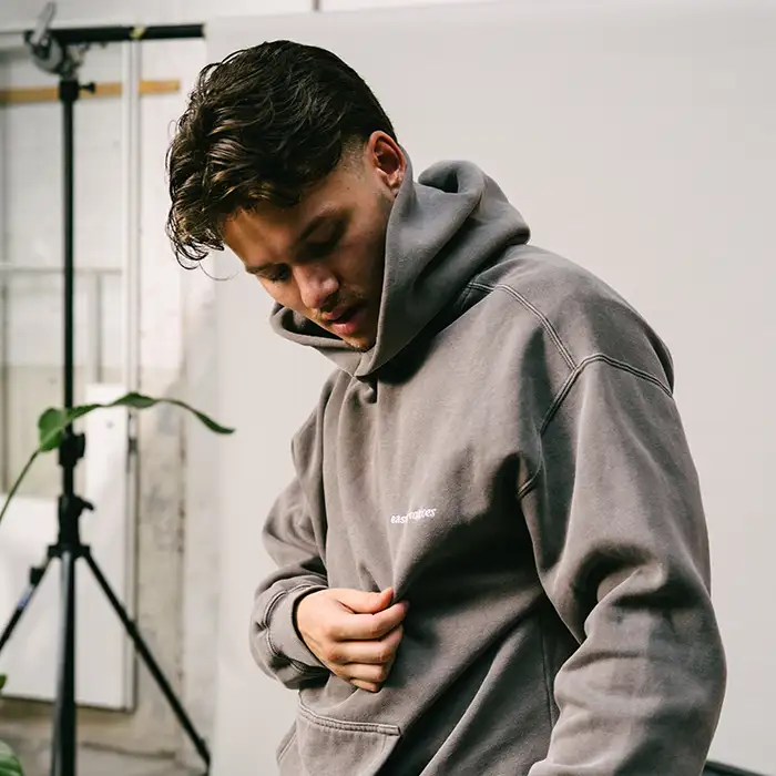 Victor van East Creatives in een grijze hoodie met het logo van het bureau, kijkend naar beneden tijdens een casual moment in de studio.