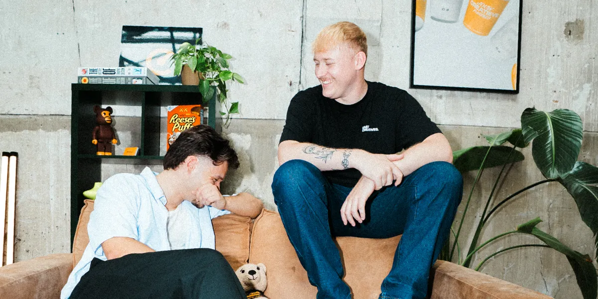 Victor en Nick van East Creatives lachend samen op de bank in hun creatieve studio in Enschede.
