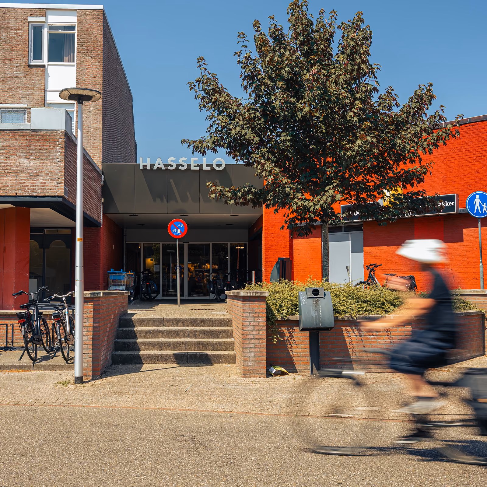 Buitengevel van Winkelcentrum Hasselo in Hengelo met logo, boom en overstekende fietser