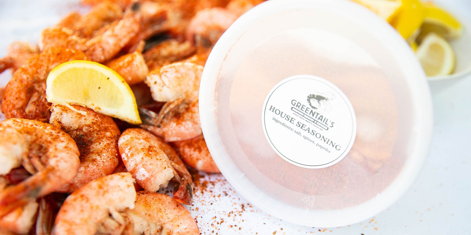 Seasoned shrimp with a lemon wedge next to a container of Greentail's House Seasoning.