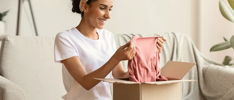 A woman holding a pink shirt in a box.