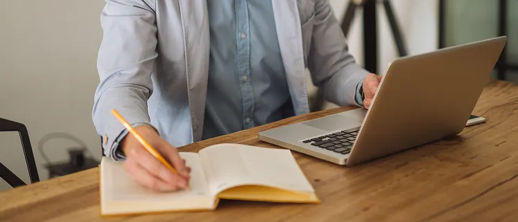 A person sitting at a table with a laptop and a notebook.