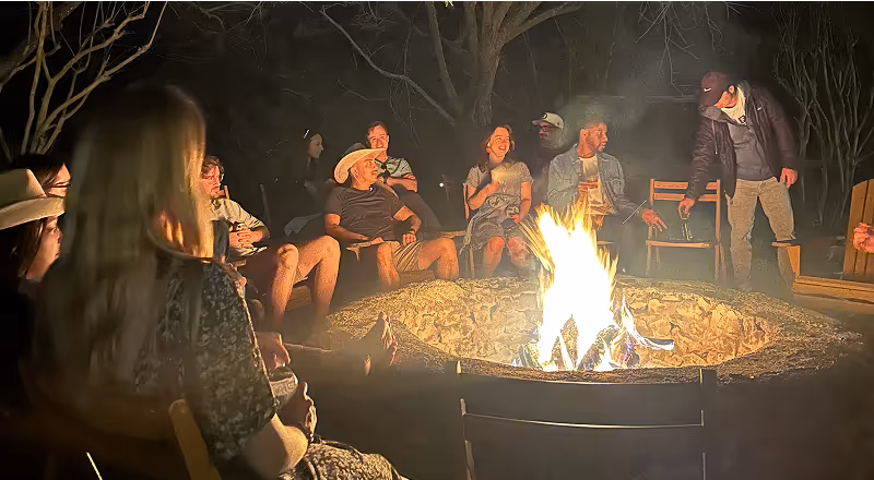 People sitting around a campfire at night playing guitar and talking