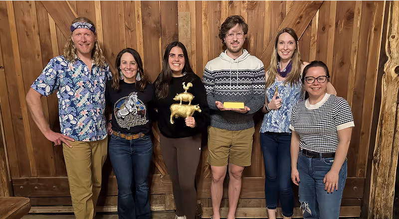 Group of people posing together indoors against a wooden wall