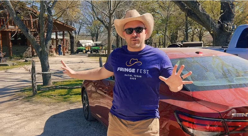 Man smiling and gesturing near a red car in a sunny parking area