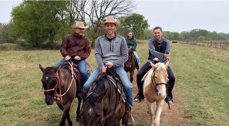 Group riding horses on a grassy trail surrounded by trees