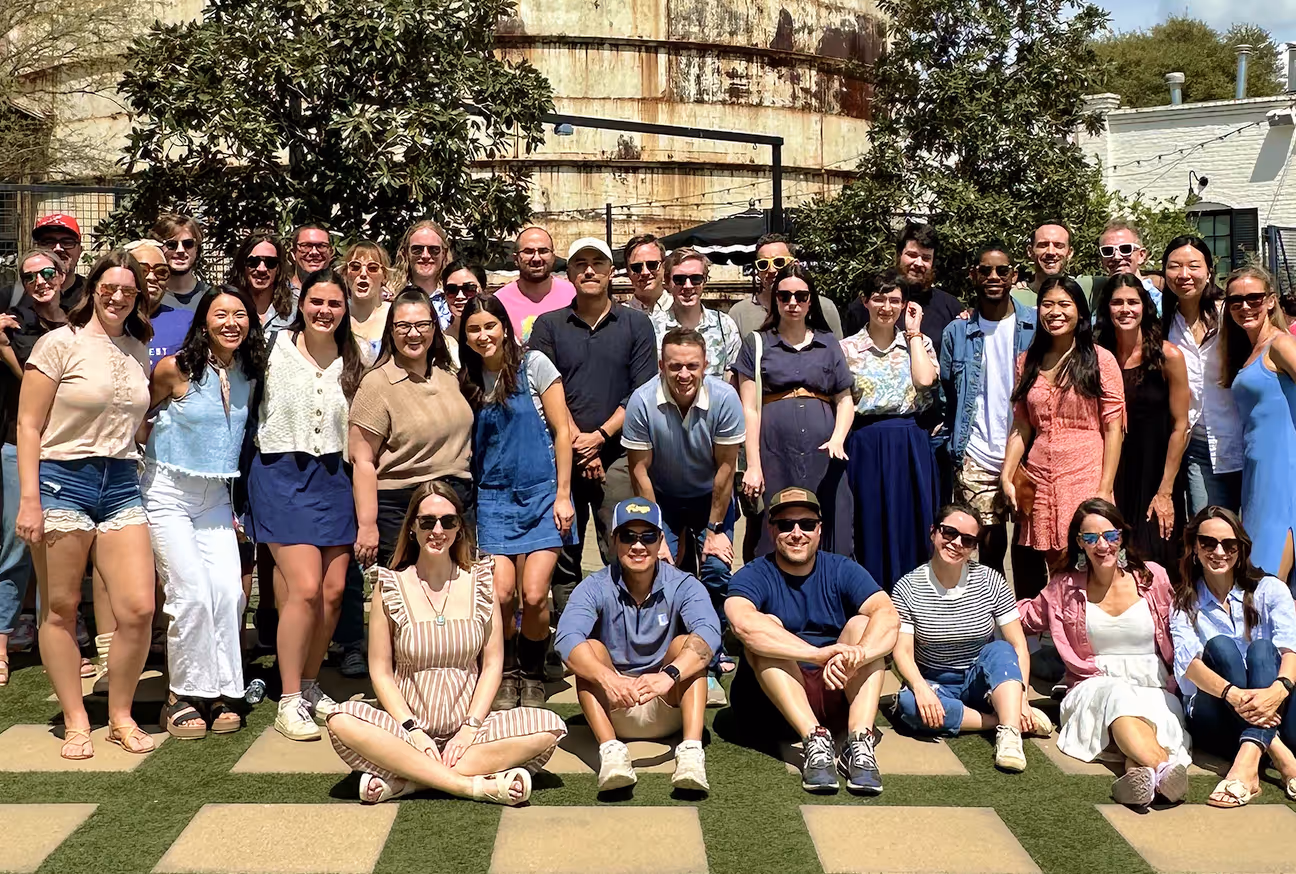 A group photo of the company team posing outdoors on a sunny day, smiling together in front of a rustic building, representing the friendly and collaborative culture featured on the About Us page.