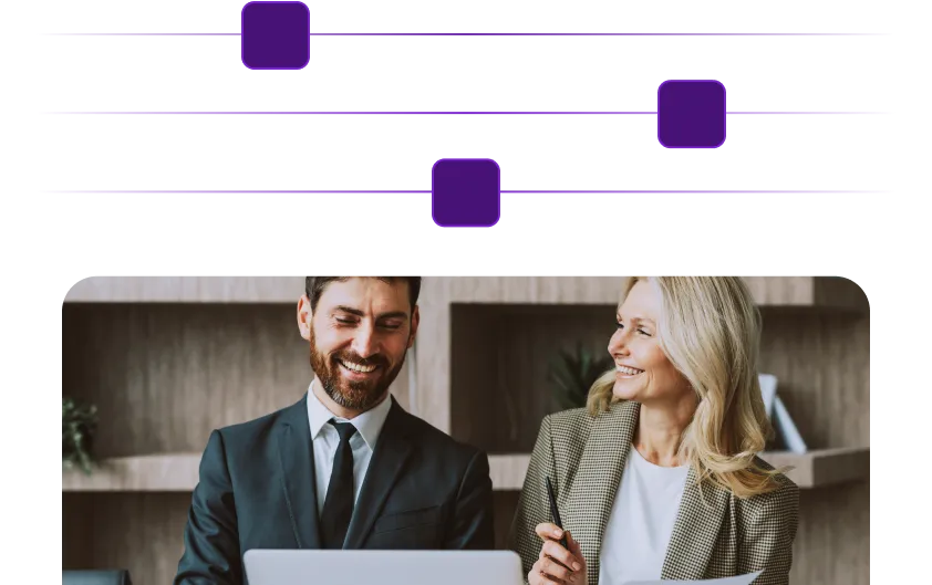 Two professionals smiling and discussing work at a laptop in an office setting.