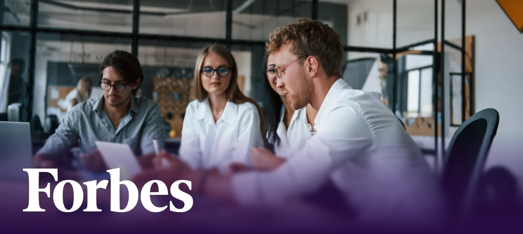 Group of four young professionals collaborating around a table in a modern office with Forbes logo overlay.