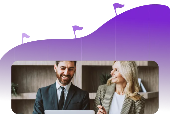 Smiling man in a suit and woman in a blazer working and discussing with a laptop in an office setting.