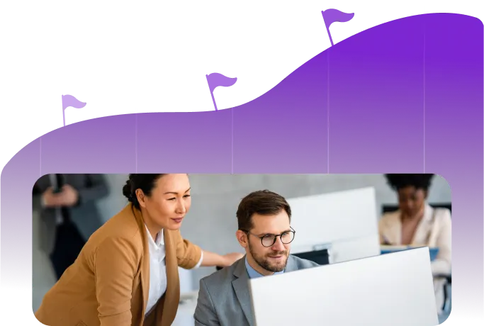 A woman in a brown jacket leans over a man in glasses who is seated at a computer, both focused on the screen, with a purple graph-like background featuring flag markers.