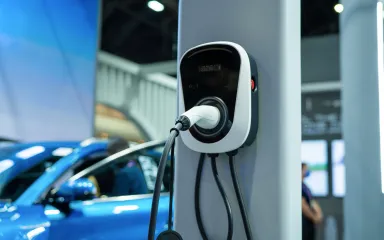 Electric vehicle charging station with a charging cable plugged in, near a blue car indoors.