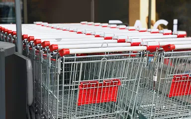 Rows of empty shopping carts with red handles lined up outside a store.