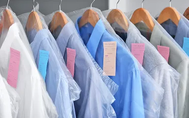 Closely lined dry-cleaned shirts in garment bags with tags on wooden hangers.