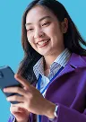 Smiling woman with long dark hair using a smartphone, wearing a purple sweater and blue collared shirt.