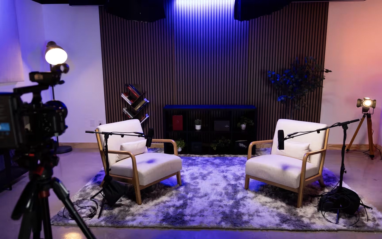 Studio de podcast moderne avec micros professionnels, casque audio, caméra, lumières et table de mixage.