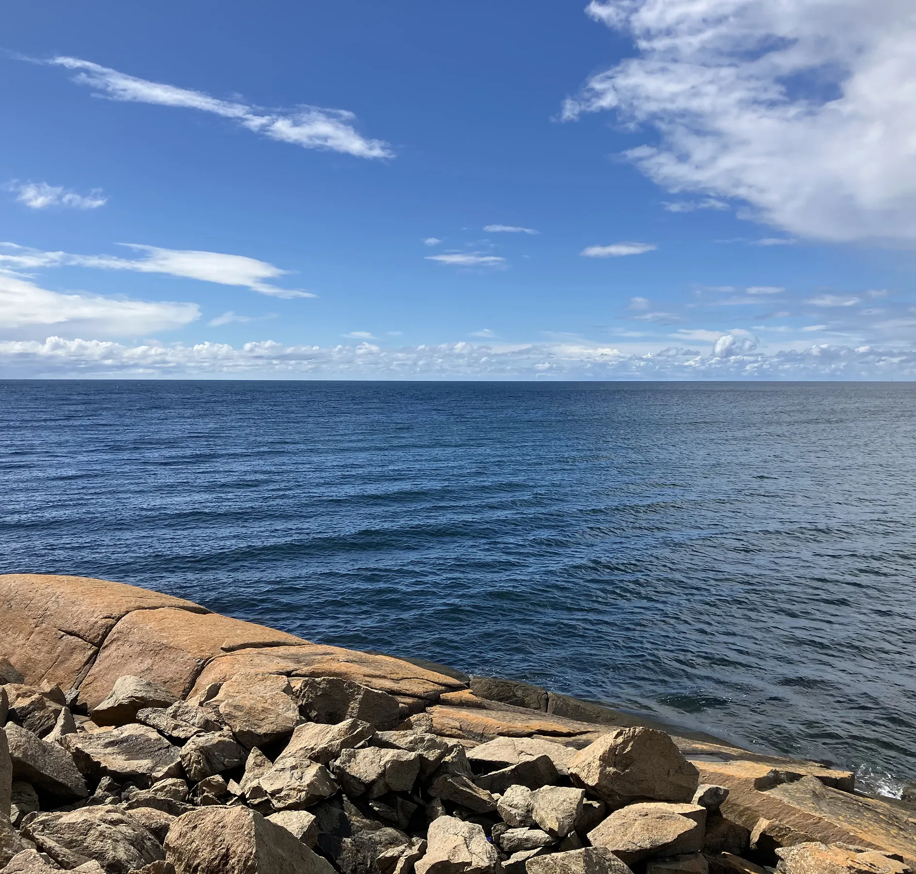 Blaues Meer im Hintergrund, vorne gelbe und braune Steine, blauer Himmel.