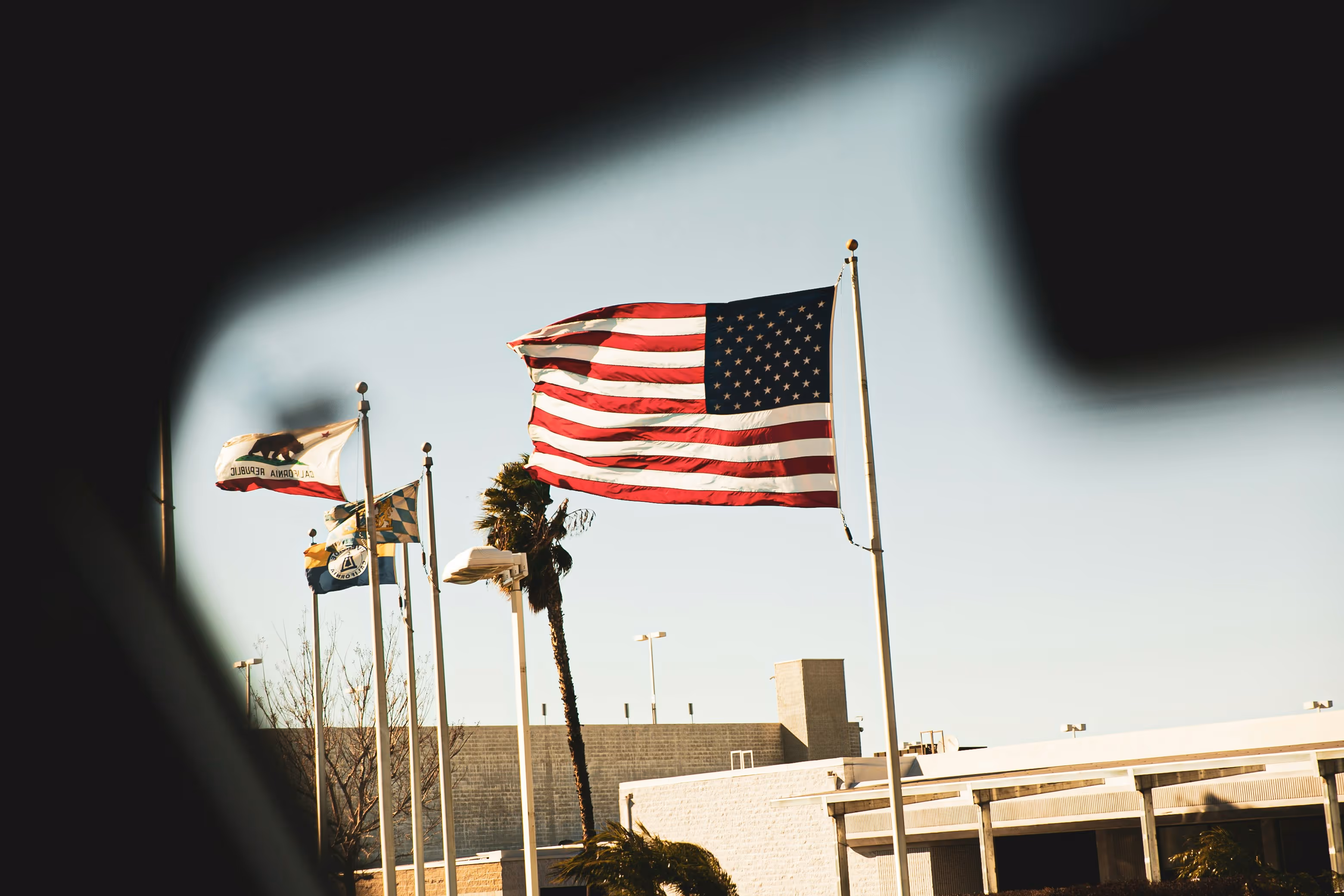 American flag and other flags waving on flagpoles outside a building on a clear day.