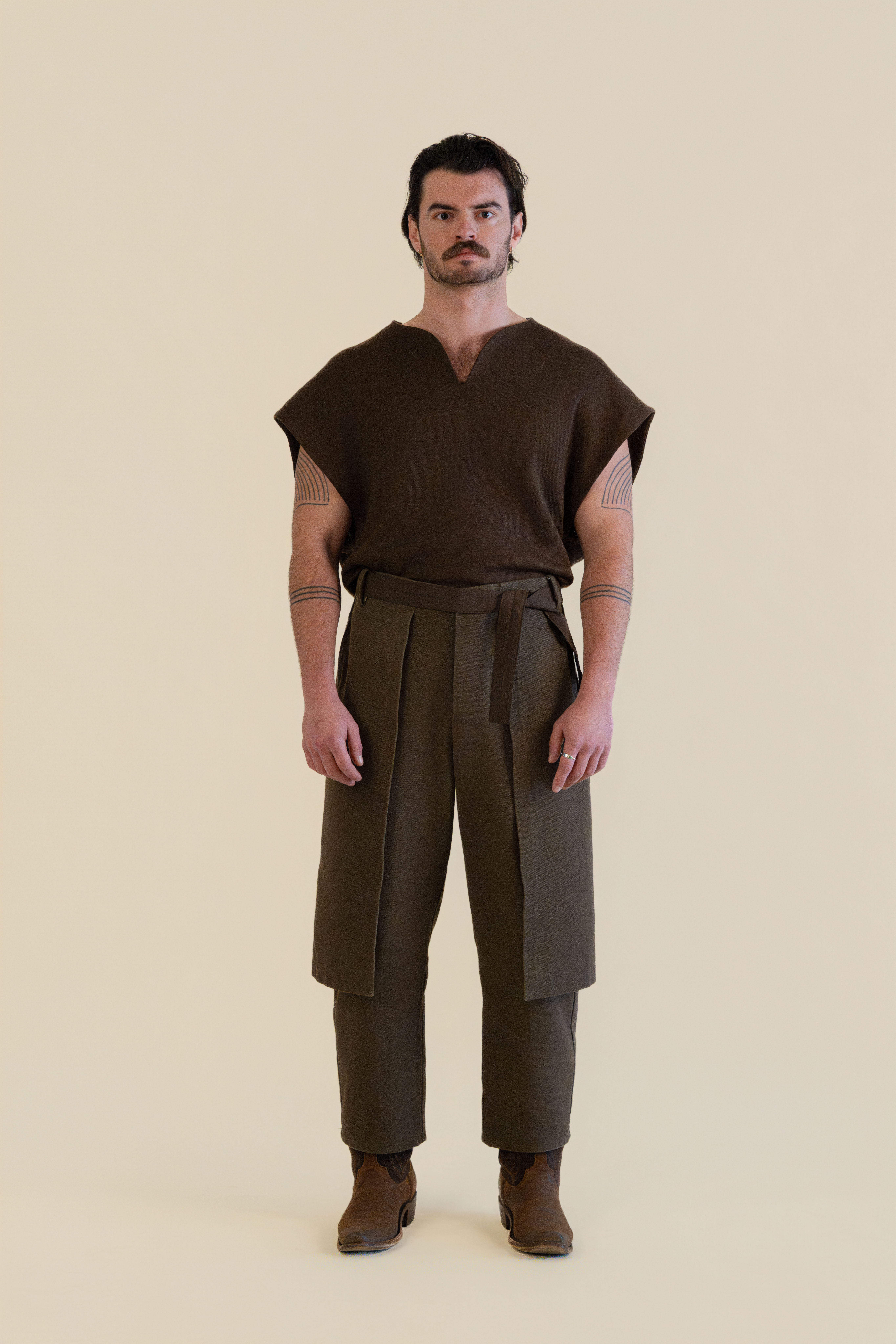 Full-body front view of male model wearing brown Cowboy Pants and brown knit top in soft warm light, Oniri editorial aesthetic