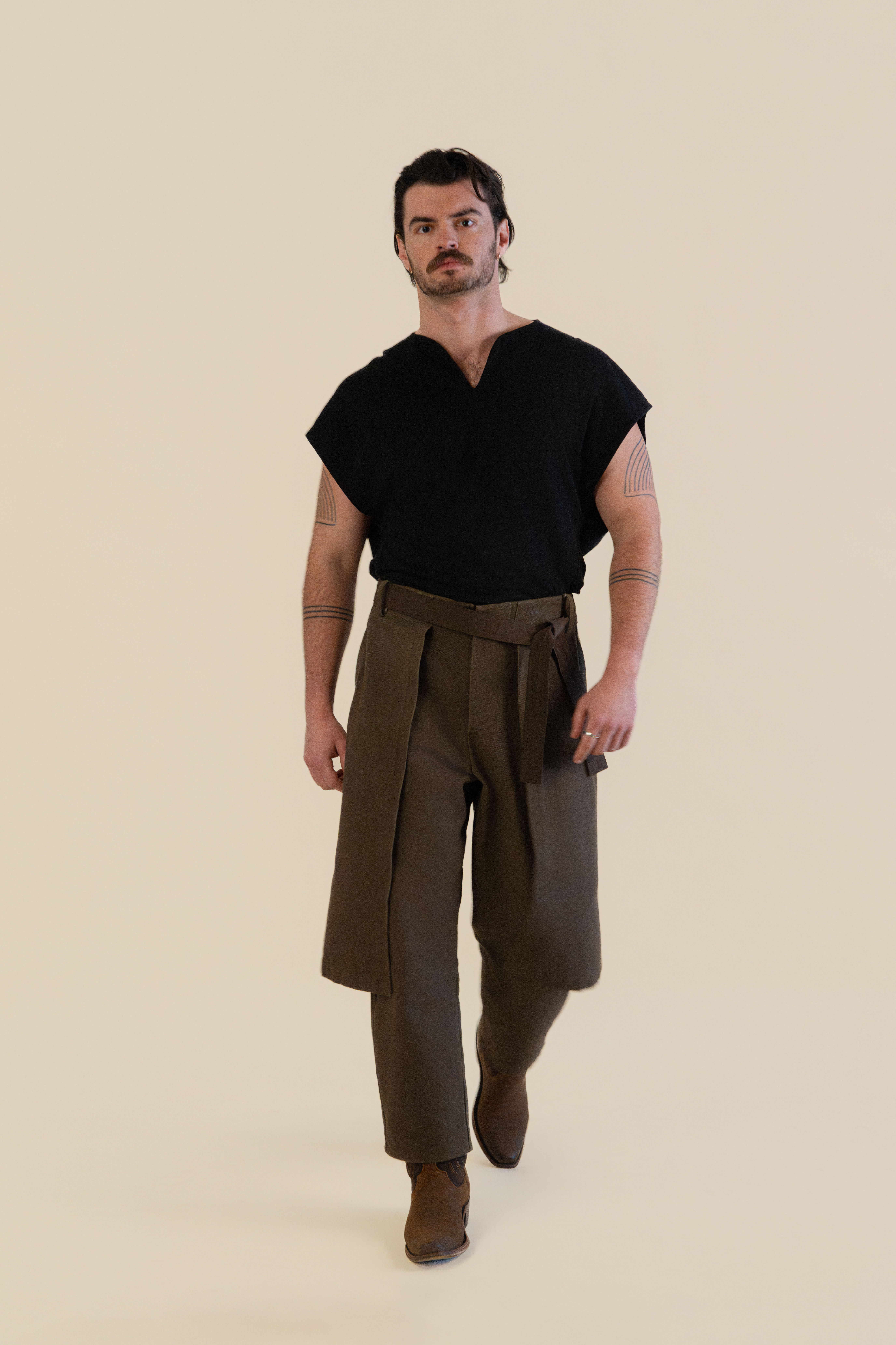 Back view of male model wearing brown Cowboy Pants in soft warm light, Oniri editorial aesthetic