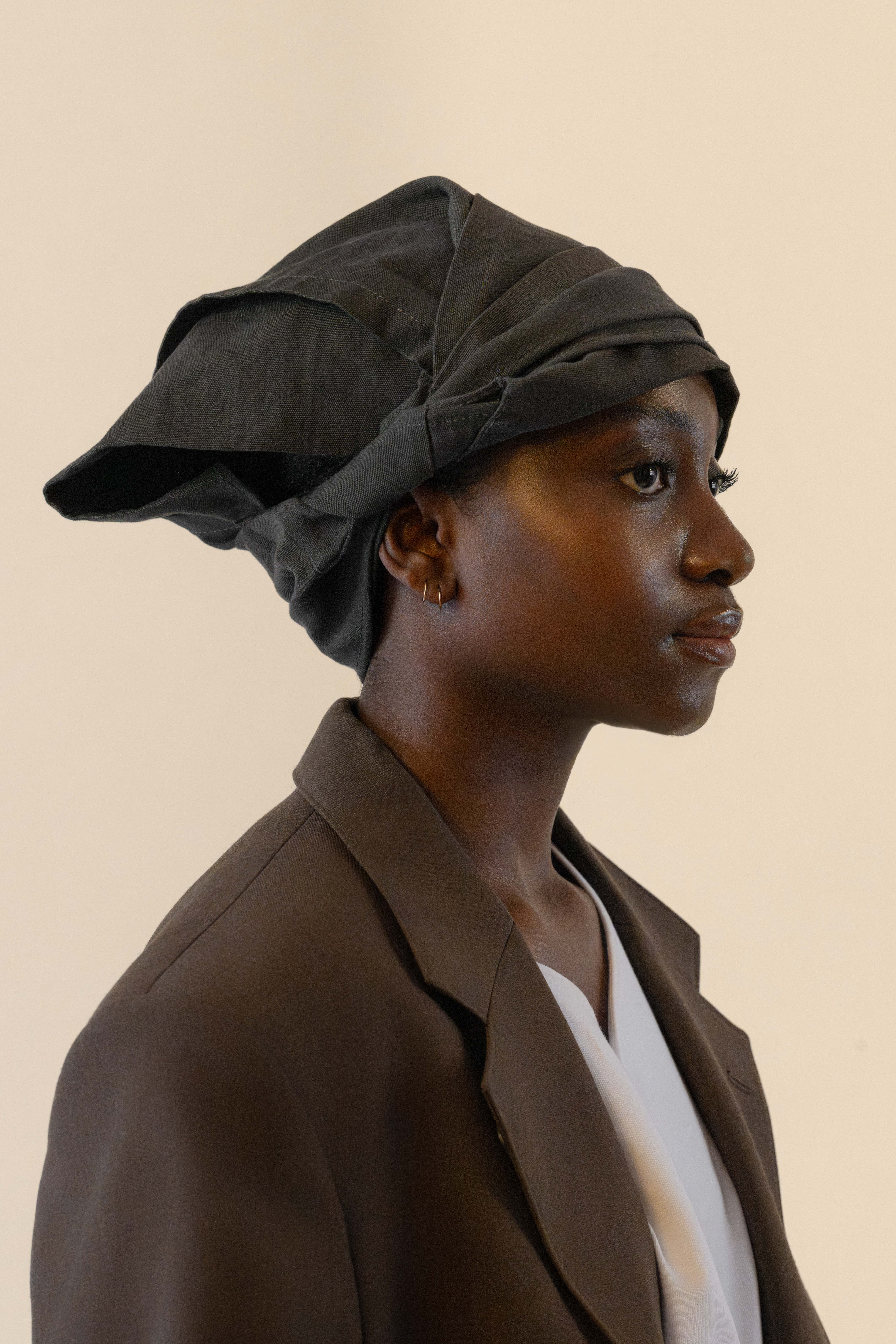 Side profile of female model wearing grey twisted bandana and brown blazer in soft warm light, Oniri editorial aesthetic