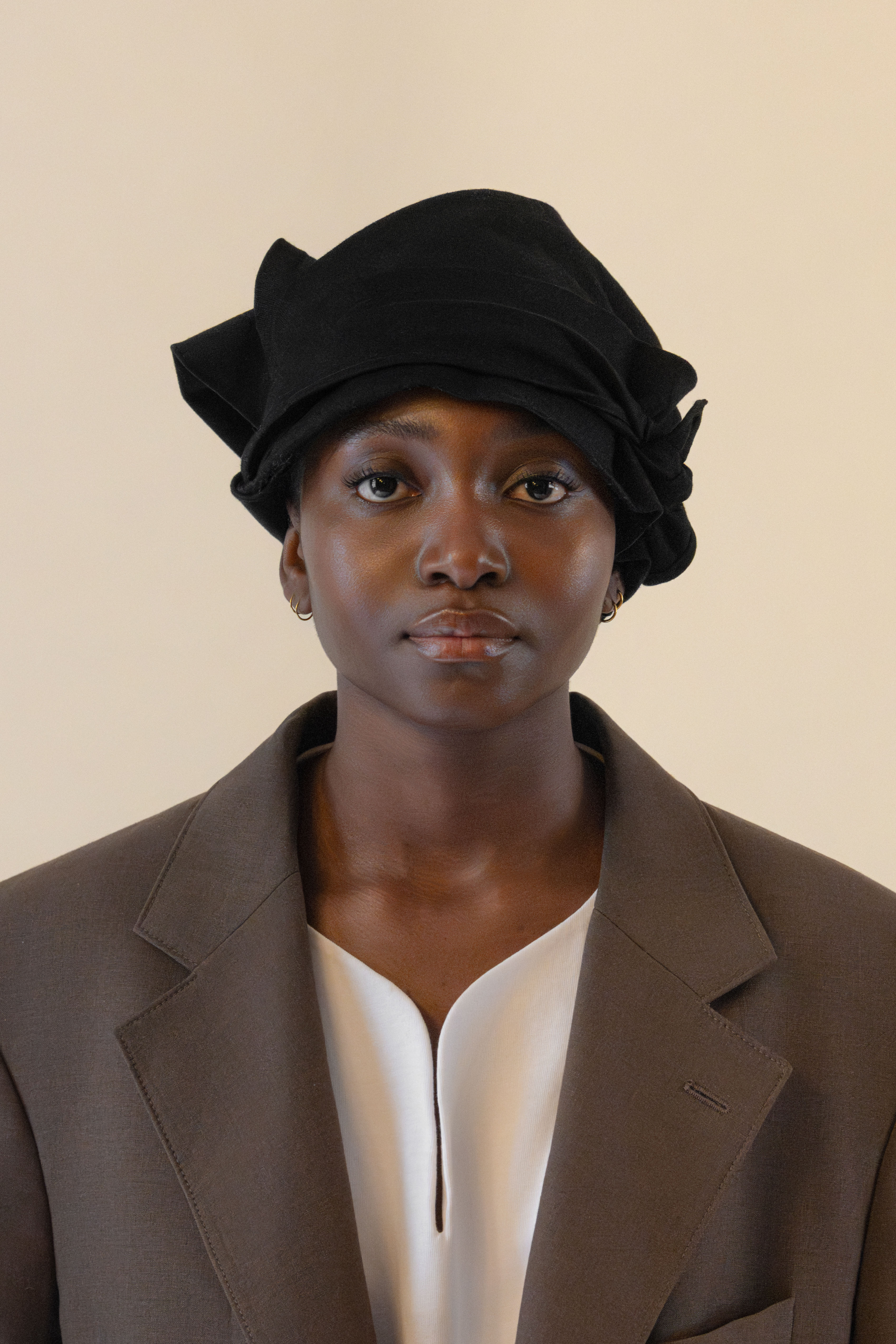 Frontal portrait of female model wearing black twisted bandana, brown blazer and white tunic in soft warm light, Oniri editorial aesthetic